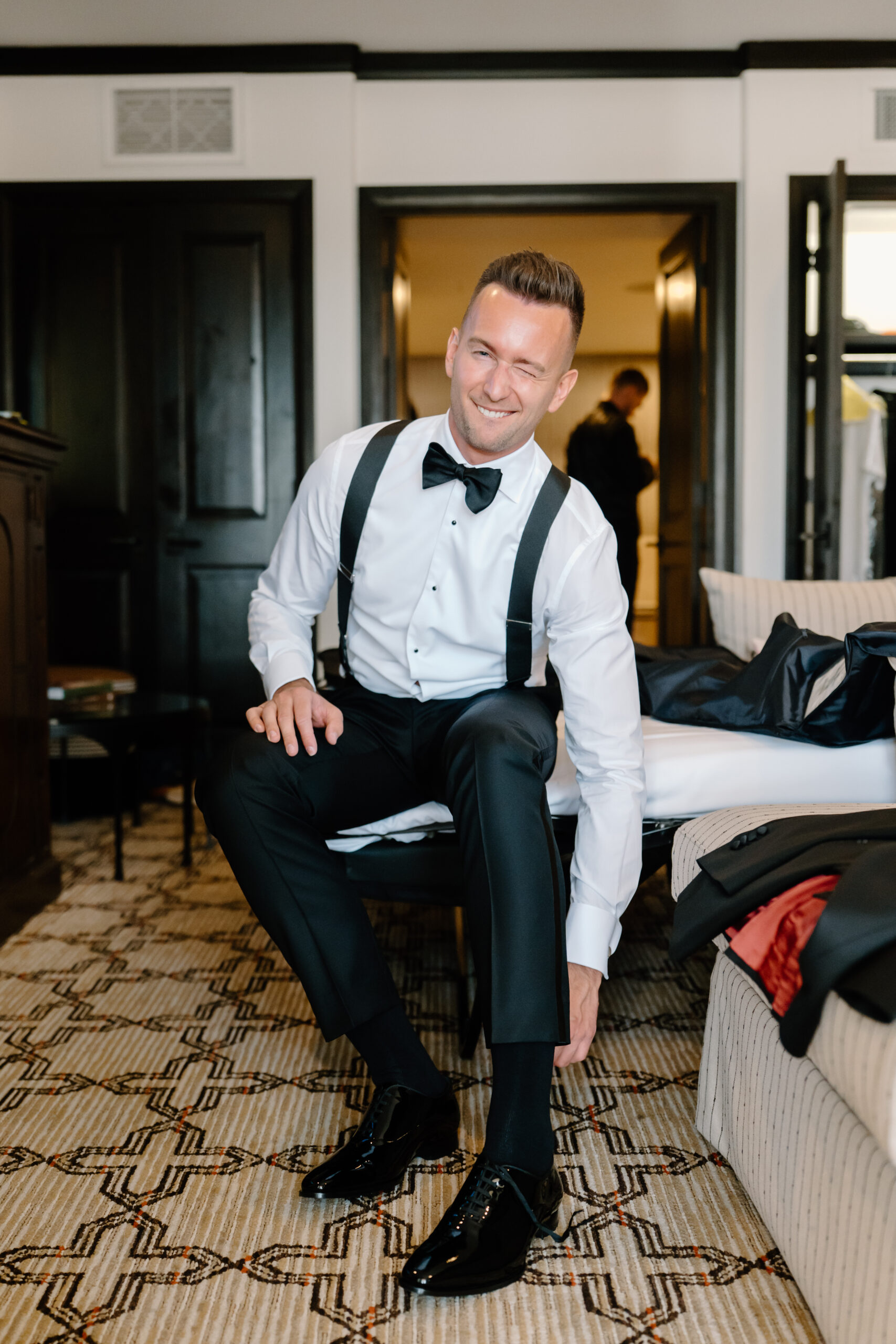 Groom getting ready and smiling as he adjusts his shoes in a hotel room before the ceremony.
