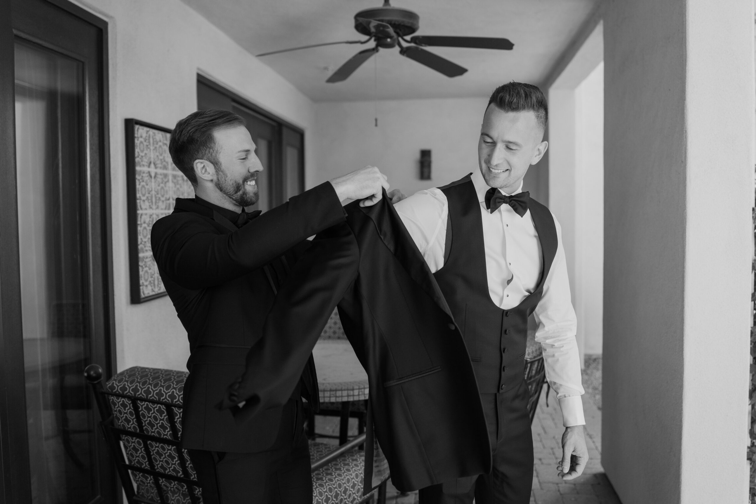 The groom laughs as his best man helps him into his suit jacket before the ceremony.