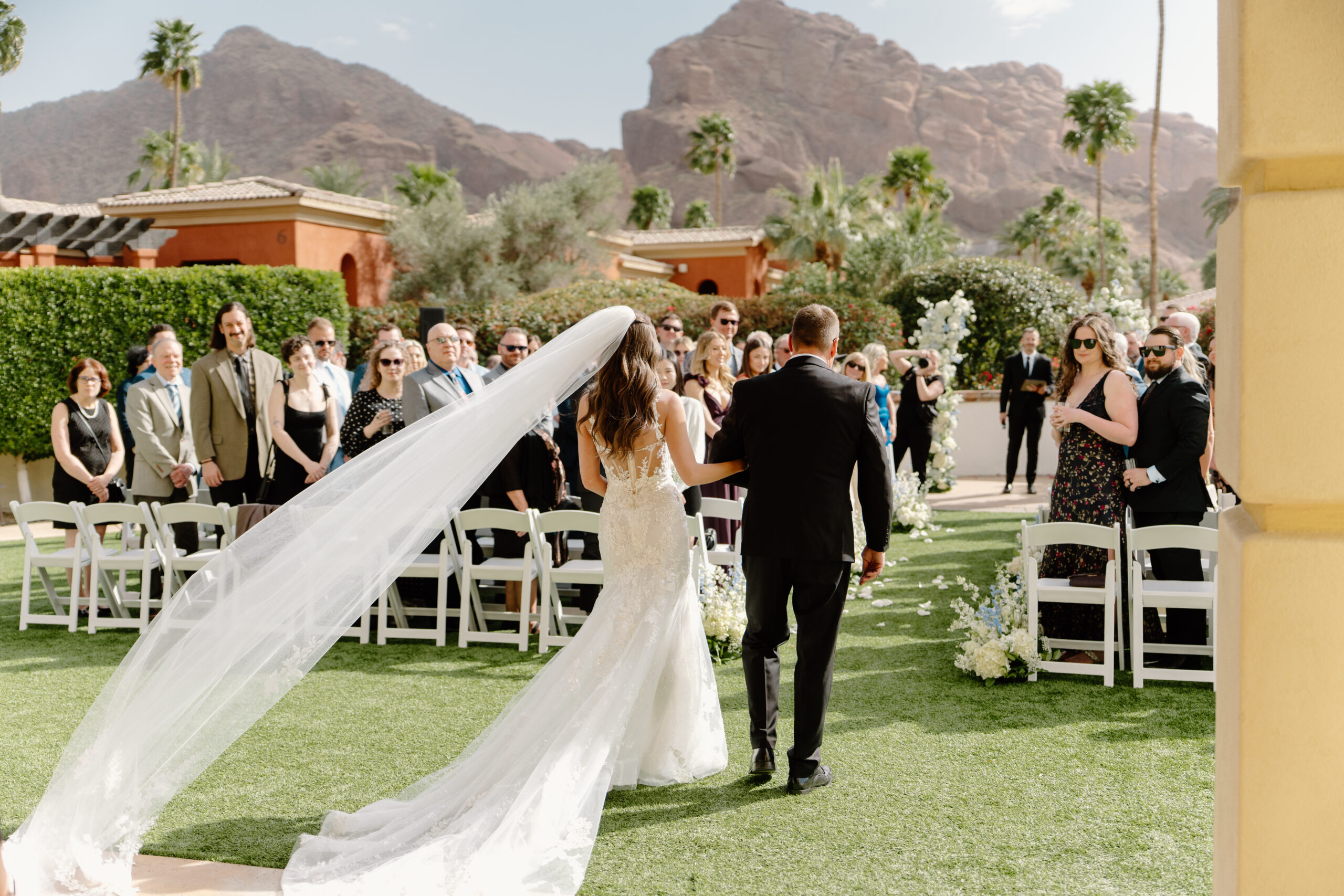 The bride walks arm in arm with her father down the aisle at Omni Montelucia, her veil flowing behind her as guests look on with the mountains in the background.