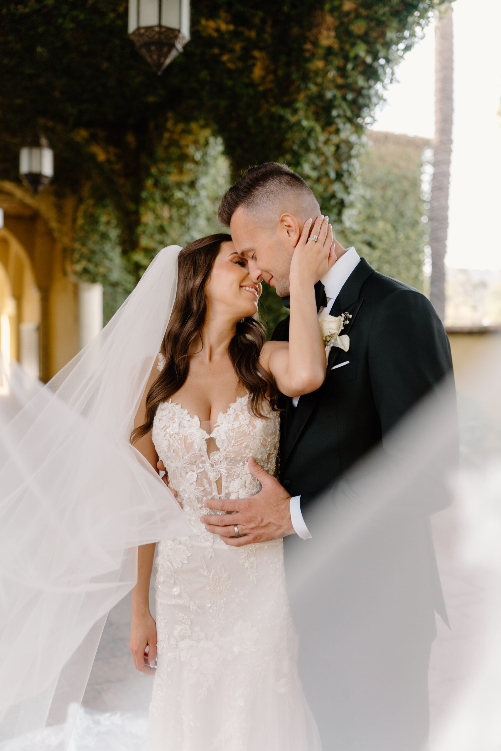 The bride and groom share an intimate moment under the ivy-covered archways at the Omni Montelucia, her veil softly blowing around them.