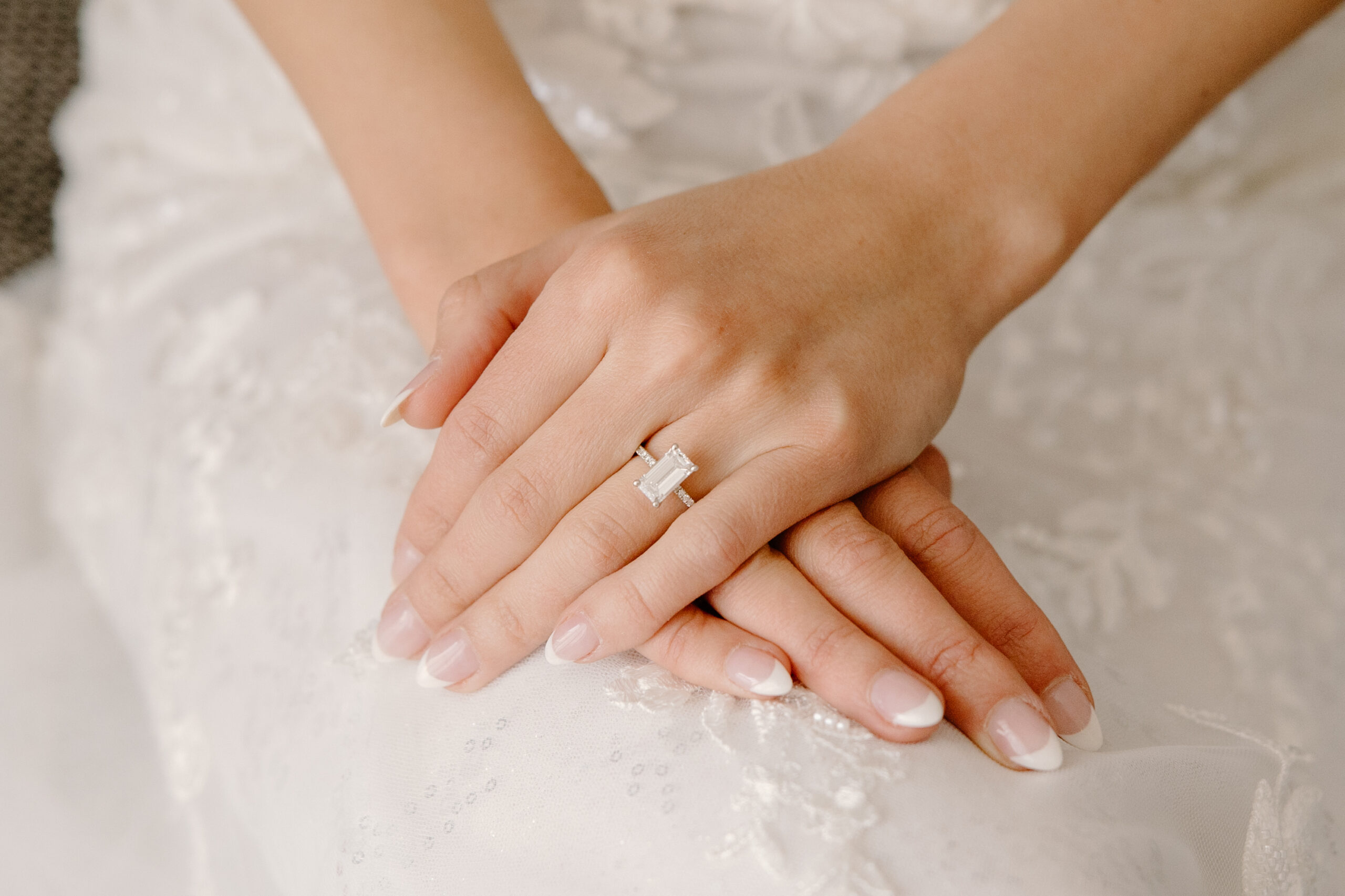 A close-up of the bride’s hands resting gently on her dress, showing her emerald-cut engagement ring.