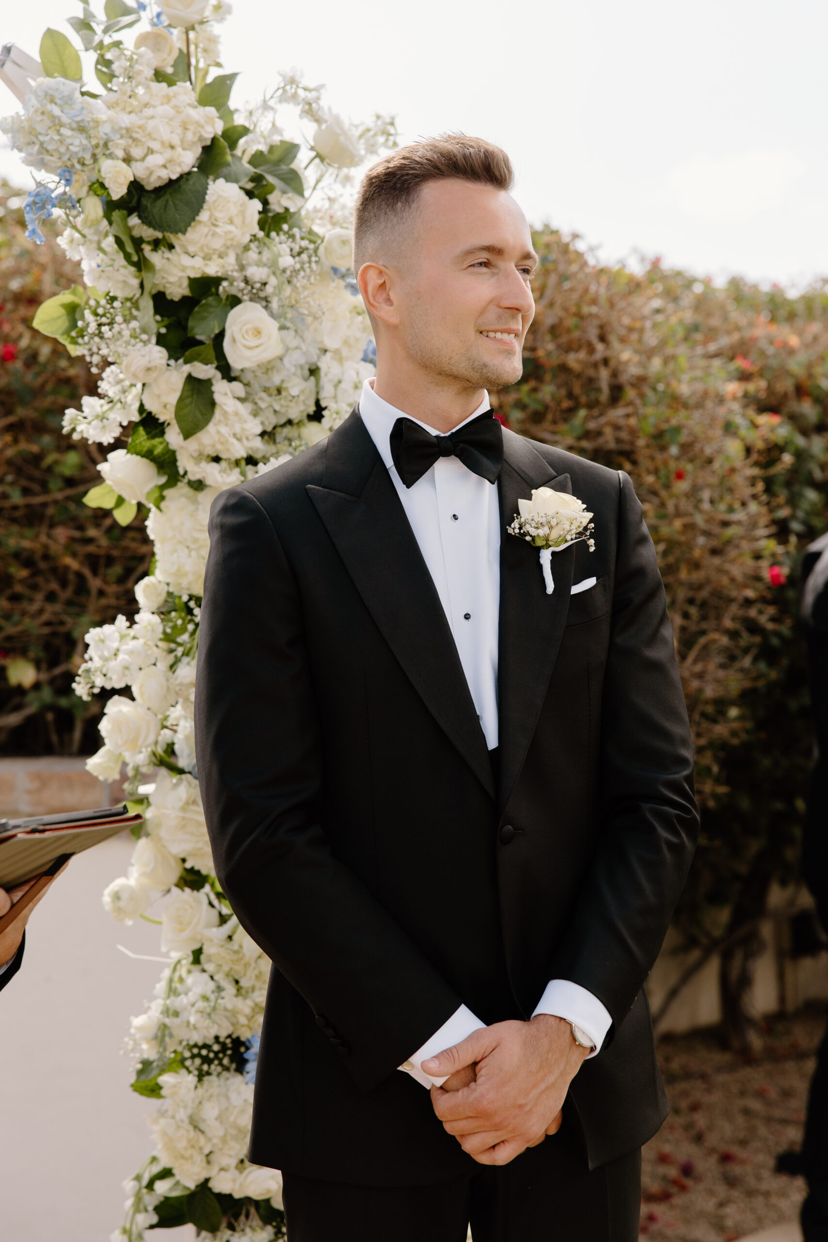 The groom smiles during their Omni Montelucia ceremony, standing before a backdrop of white and blue blooms.