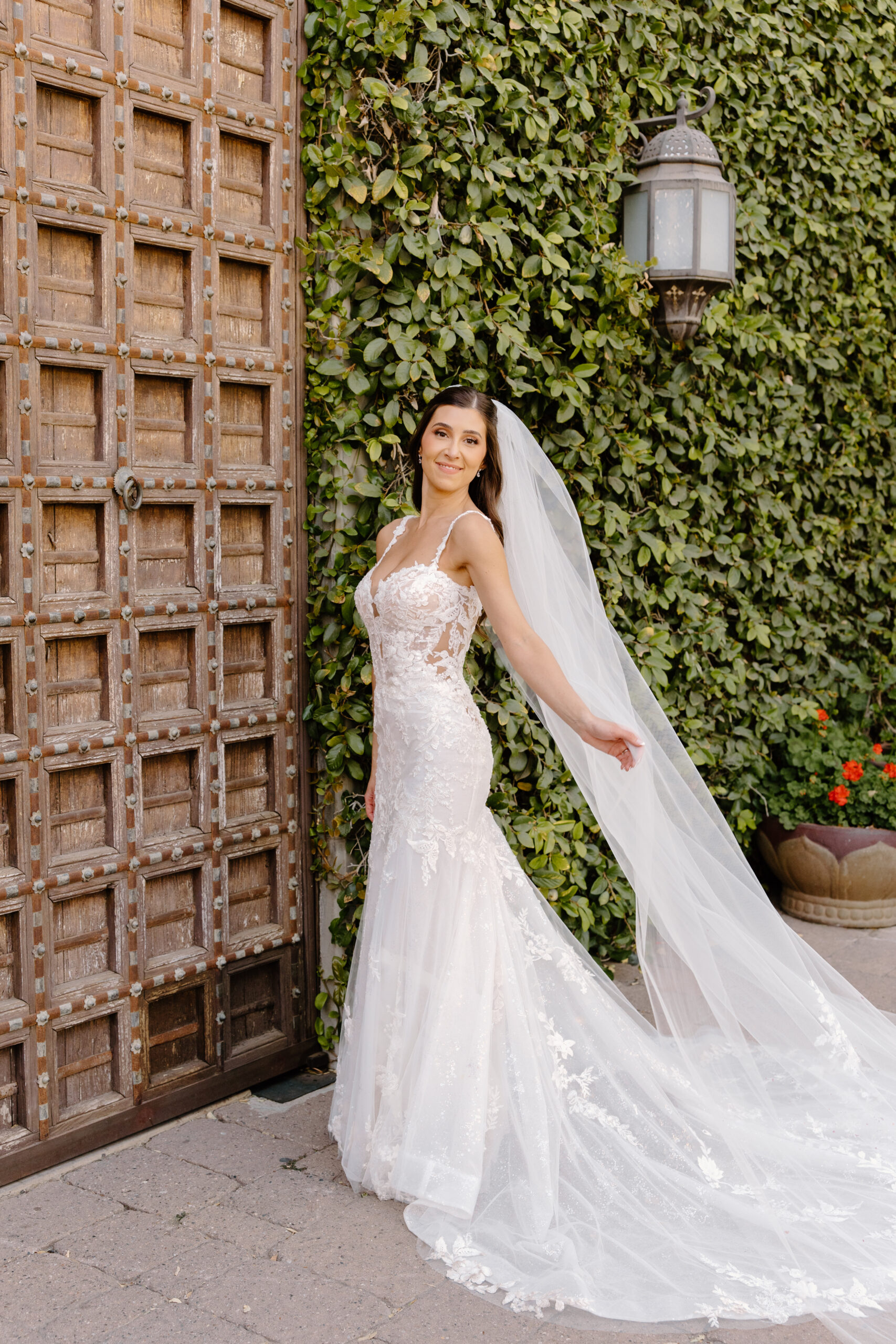 The bride twirls her veil in front of the rustic wooden doors at Omni Montelucia, surrounded by lush greenery.
