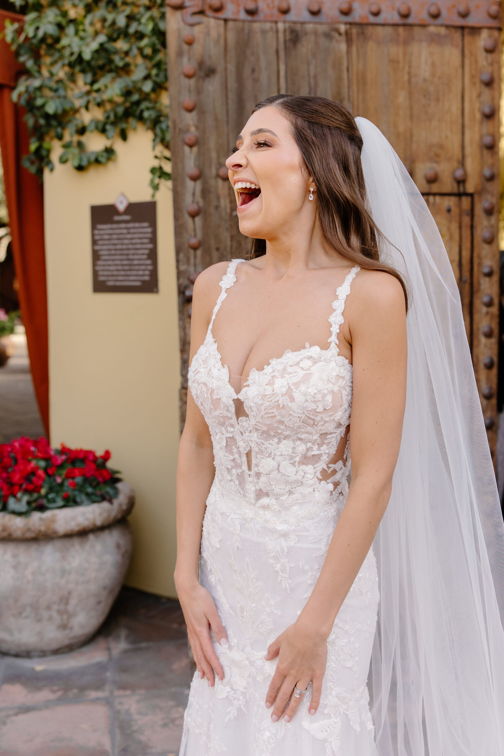 The bride laughs with pure joy in a sunny courtyard at Omni Montelucia, her lace wedding gown glowing in the light.