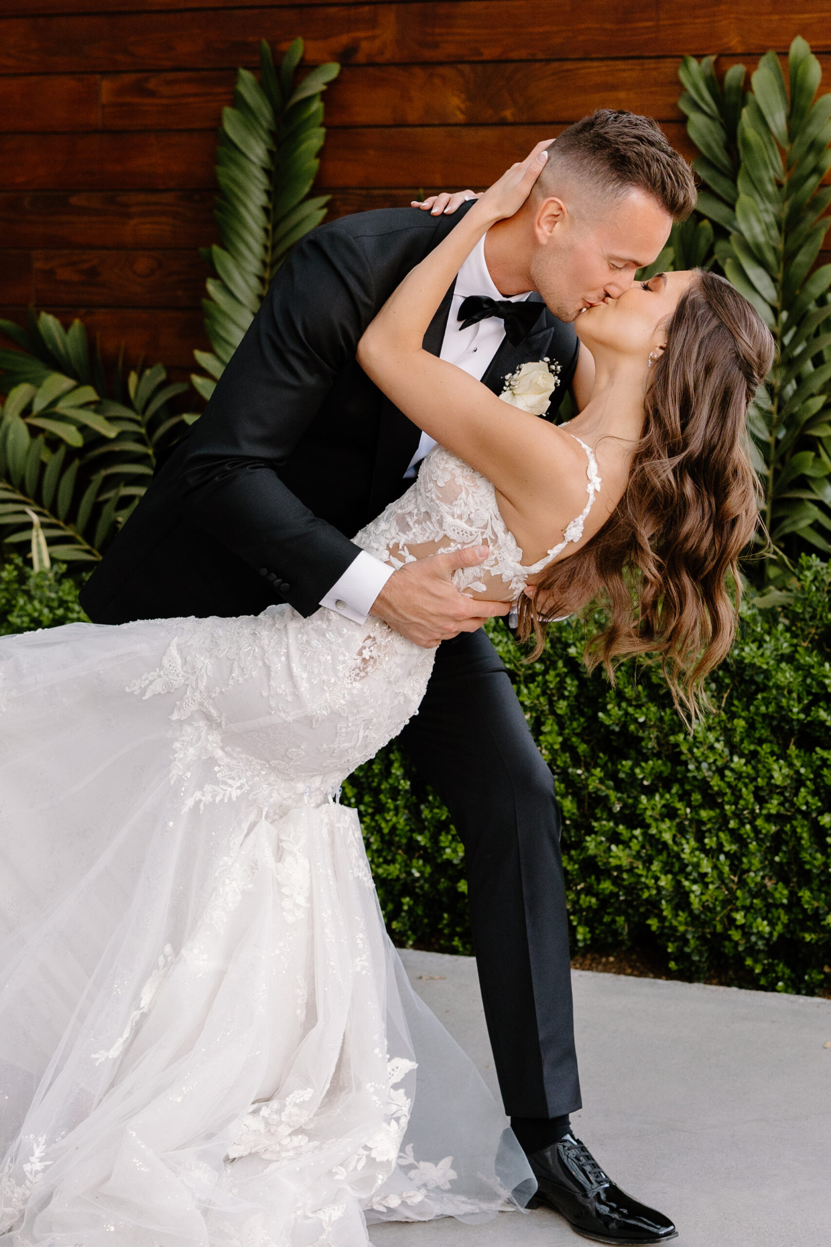 The groom dips the bride into a romantic kiss, surrounded by lush greenery and warm tones at the Omni Montelucia.