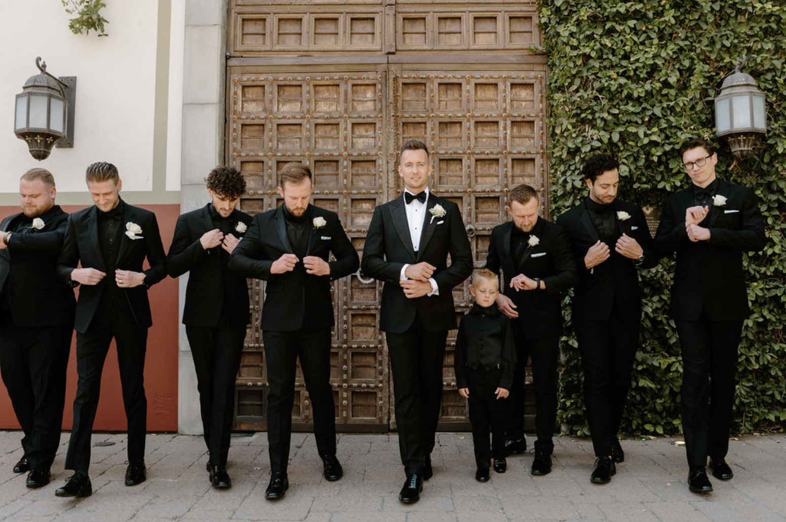 Groom and his groomsmen walking together and adjusting their suits in front of ornate wooden doors at the Omni Montelucia.