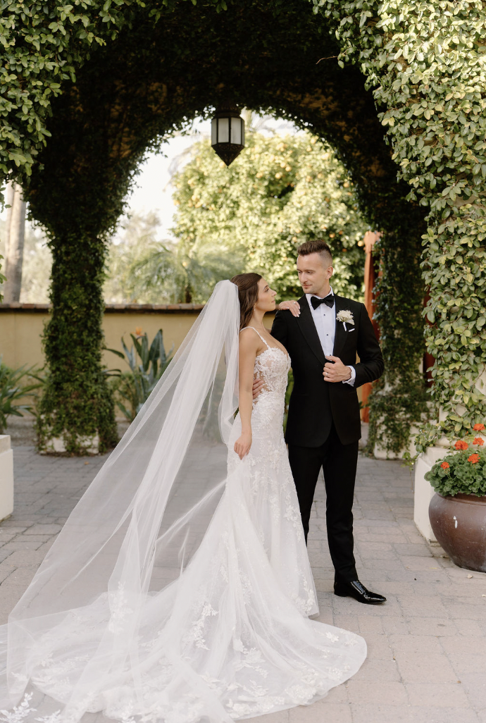Bride and groom sharing a quiet moment under an ivy-covered archway as her veil flows behind her.