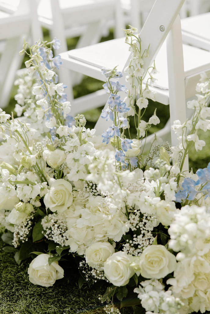 Close-up of soft white and light blue floral arrangements lining the ceremony aisle.