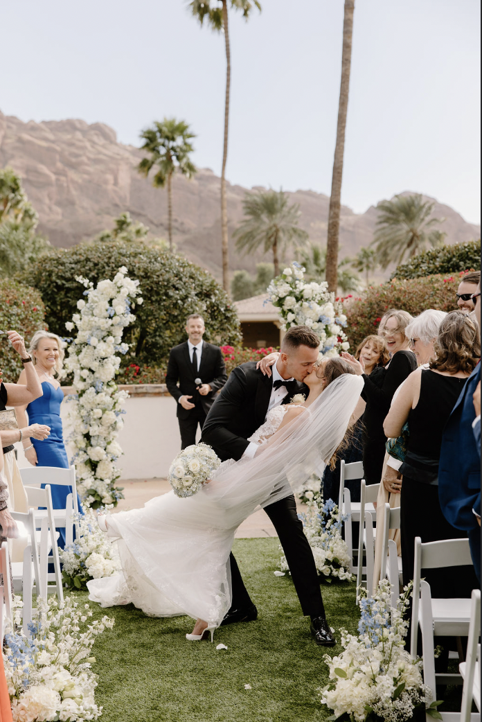 Bride and groom share a joyful dip-kiss down the aisle surrounded by guests at the Omni Montelucia.