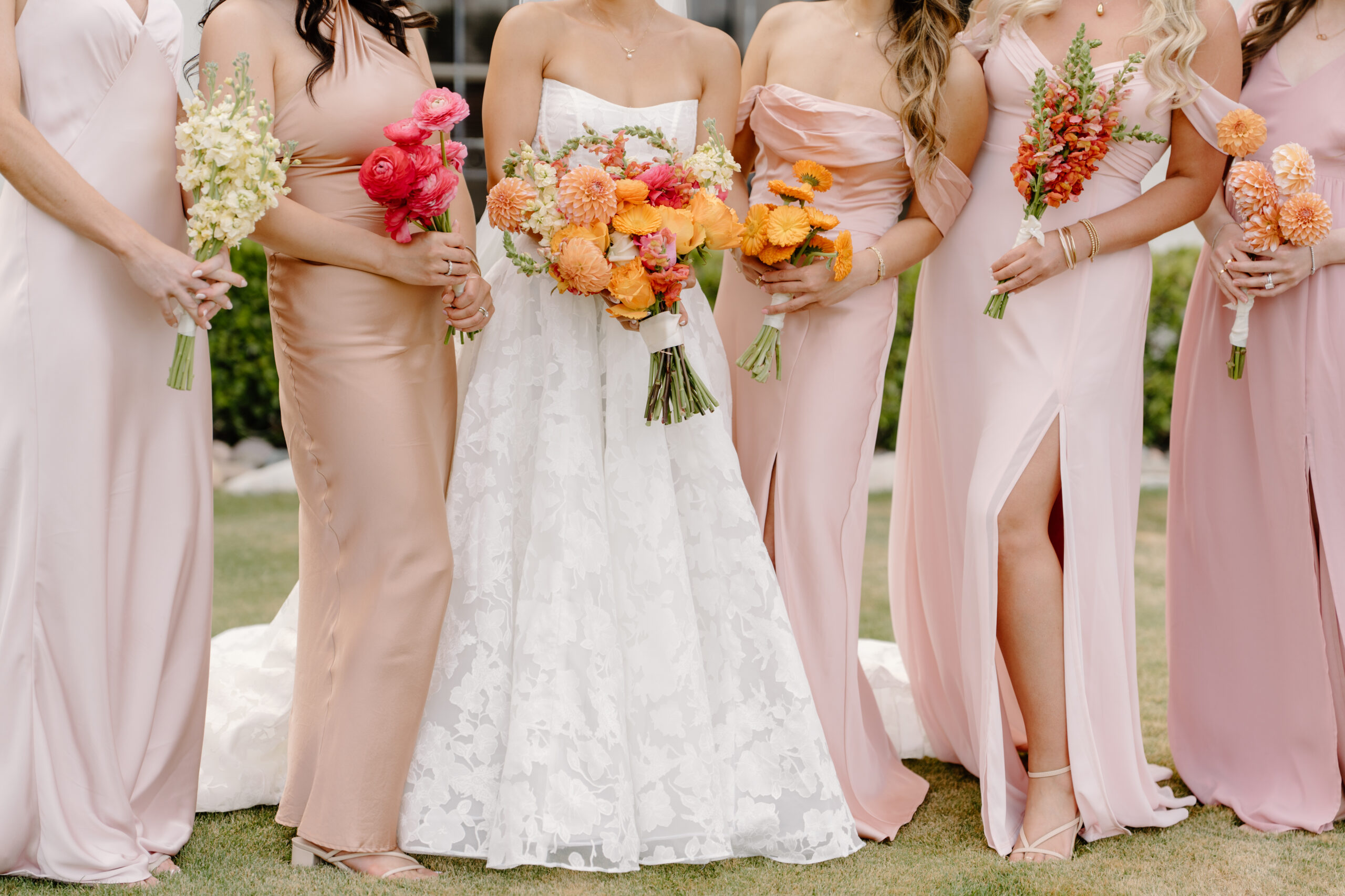 The bride and bridesmaids standing together, holding bouquets of bright orange, coral, and blush flowers at mccormick ranch golf club.