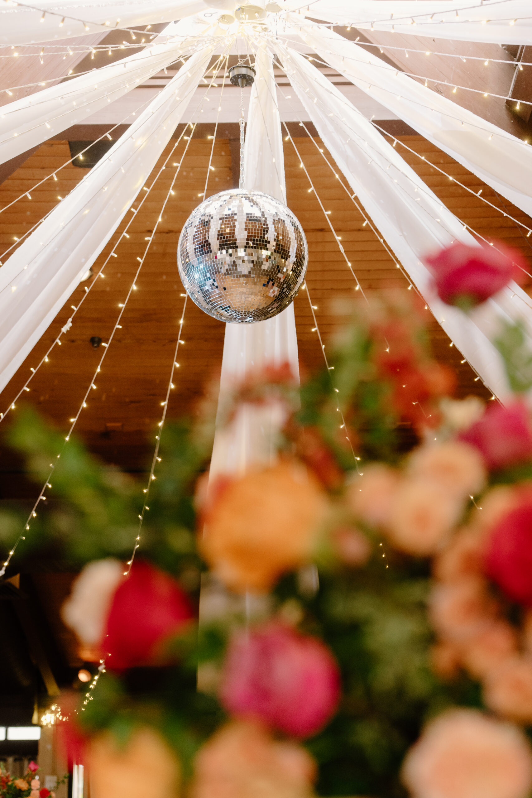 A sparkling disco ball hanging from draped white fabric and twinkle lights inside the reception space.
