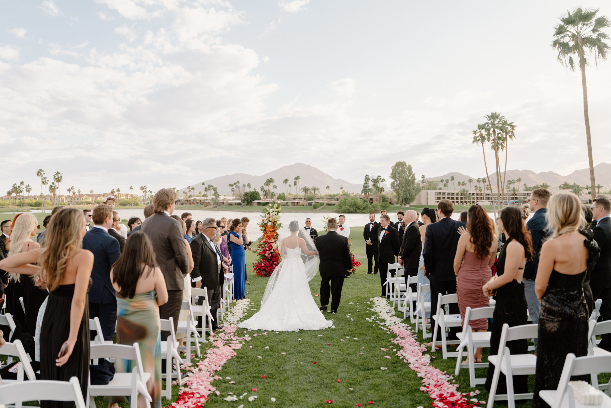 The bride walking down a petal-lined aisle toward the ceremony arch, surrounded by seated guests and mountain views.