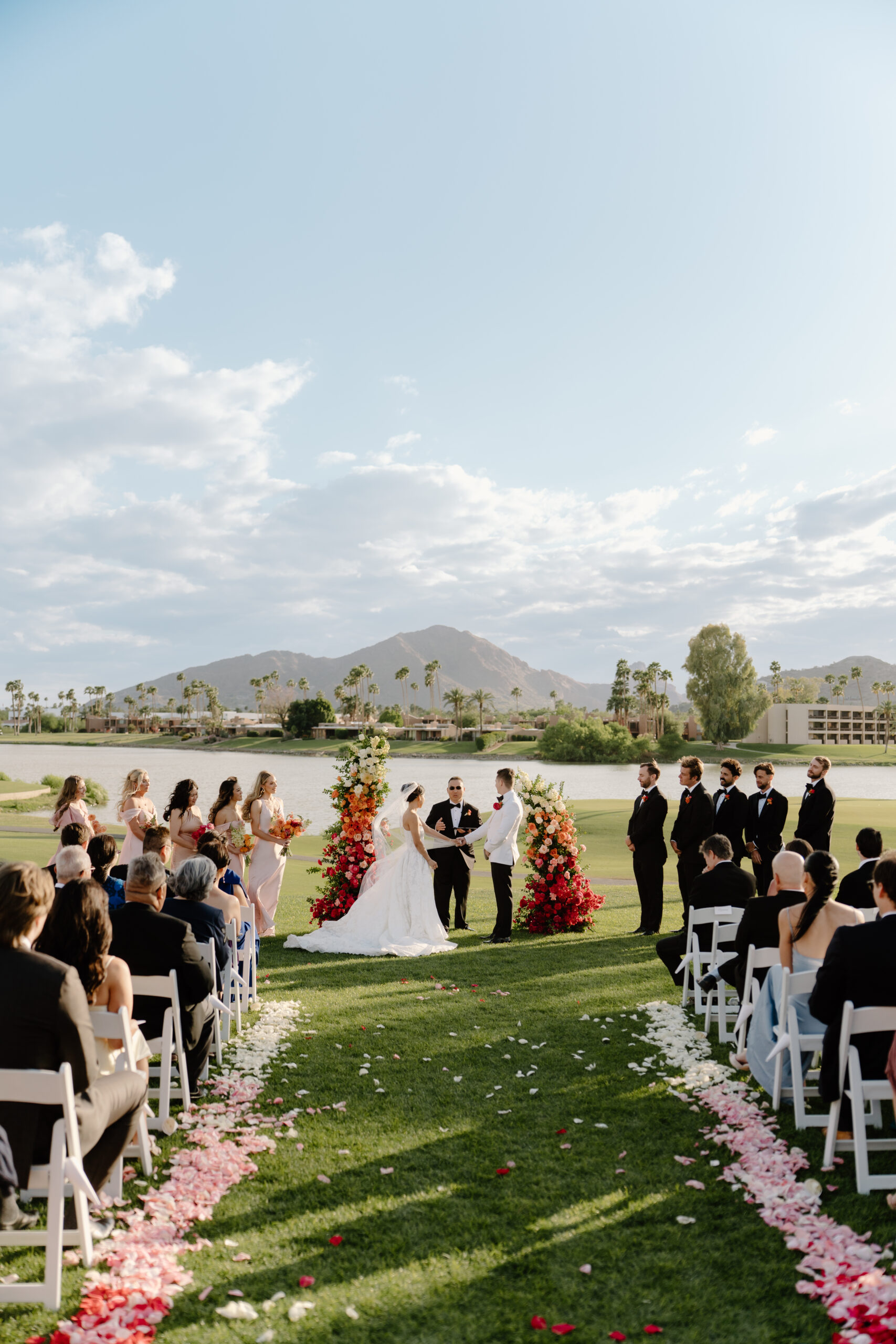 The couple standing together under two colorful floral pillars as they exchange vows at mccormick ranch golf club.