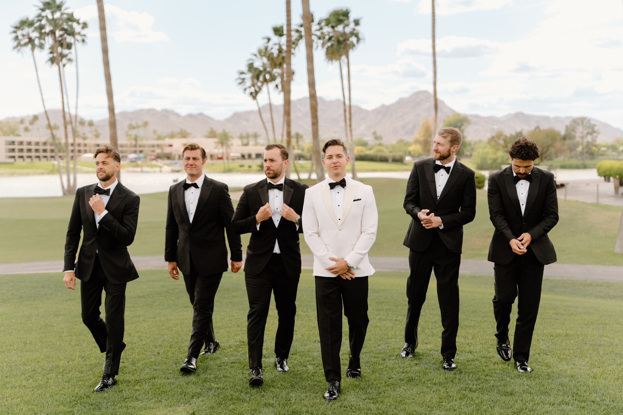The groom and his groomsmen walking confidently across the green, dressed in classic black and white tuxedos.