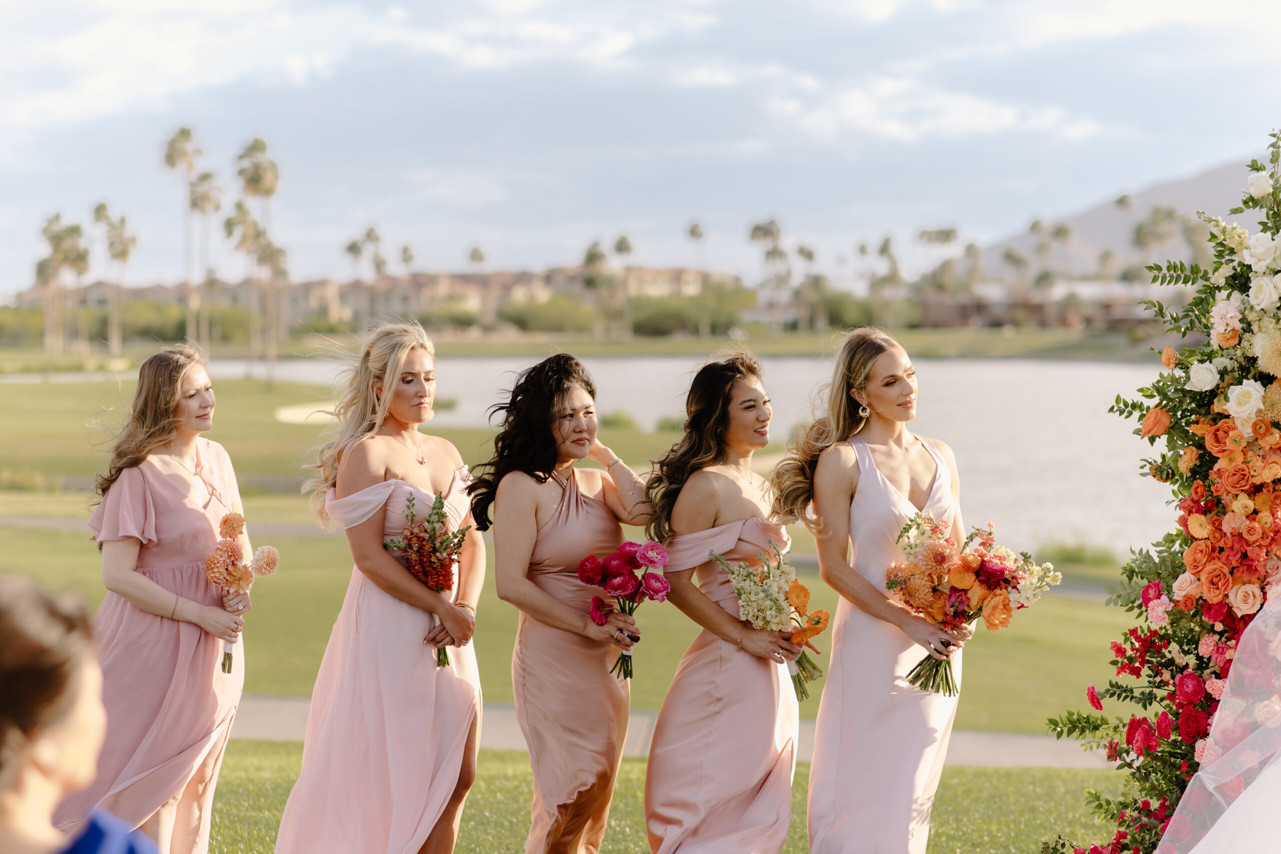 Bridesmaids in blush dresses holding bright bouquets as they stand together during the ceremony at mccormick ranch golf club.
