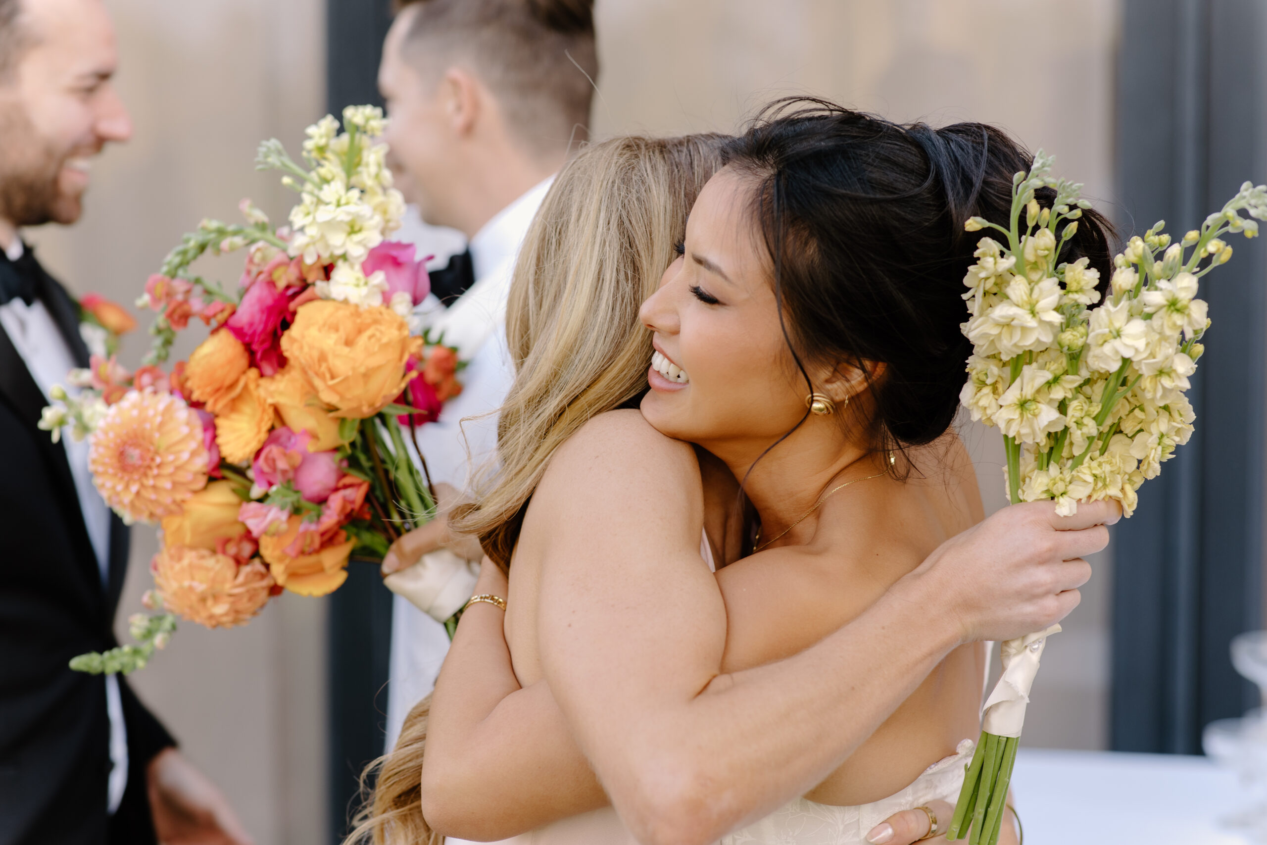 The bride hugging a guest joyfully, holding a soft yellow bouquet as the celebration continues.