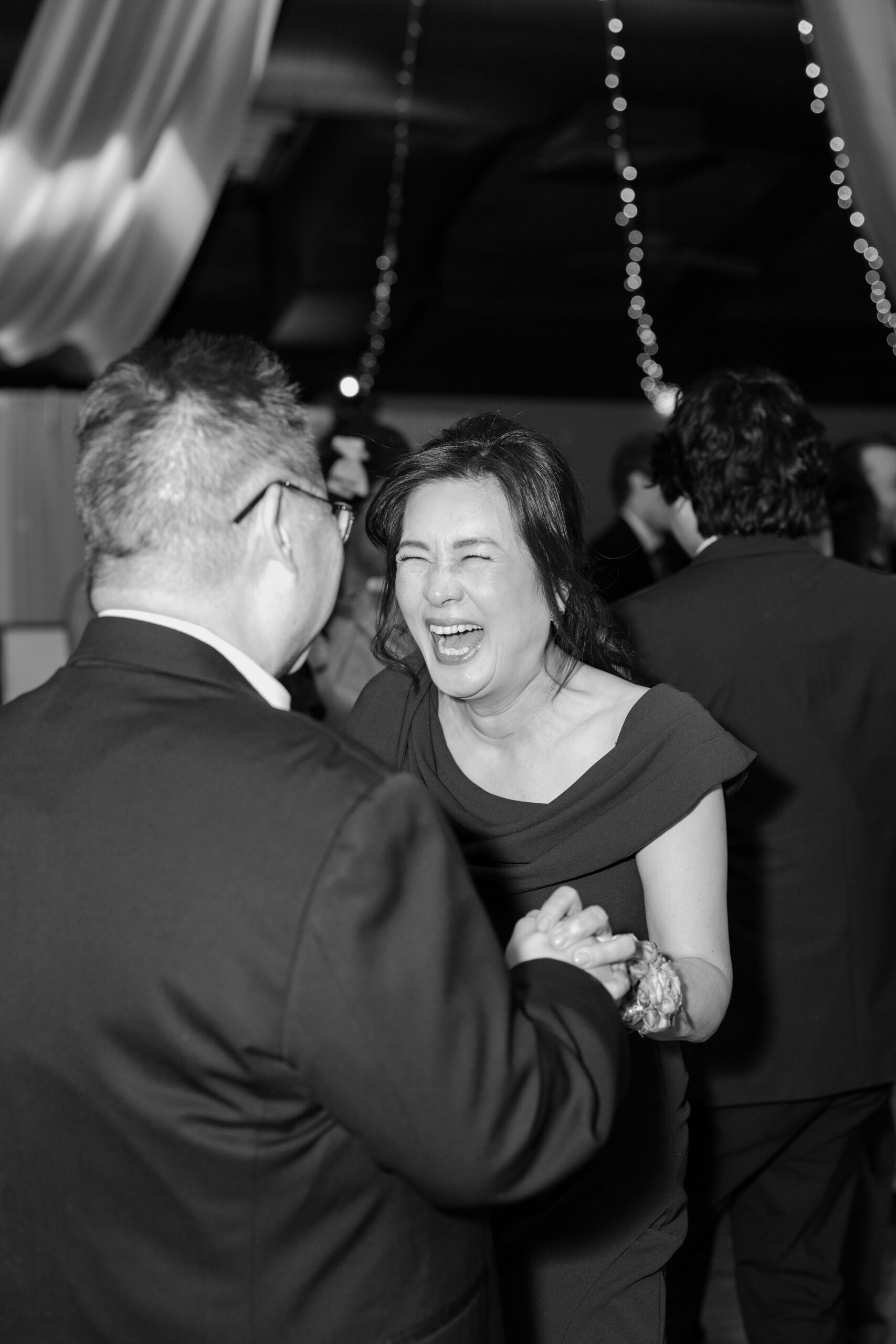 Black and white candid of guests laughing and dancing together during the reception.
