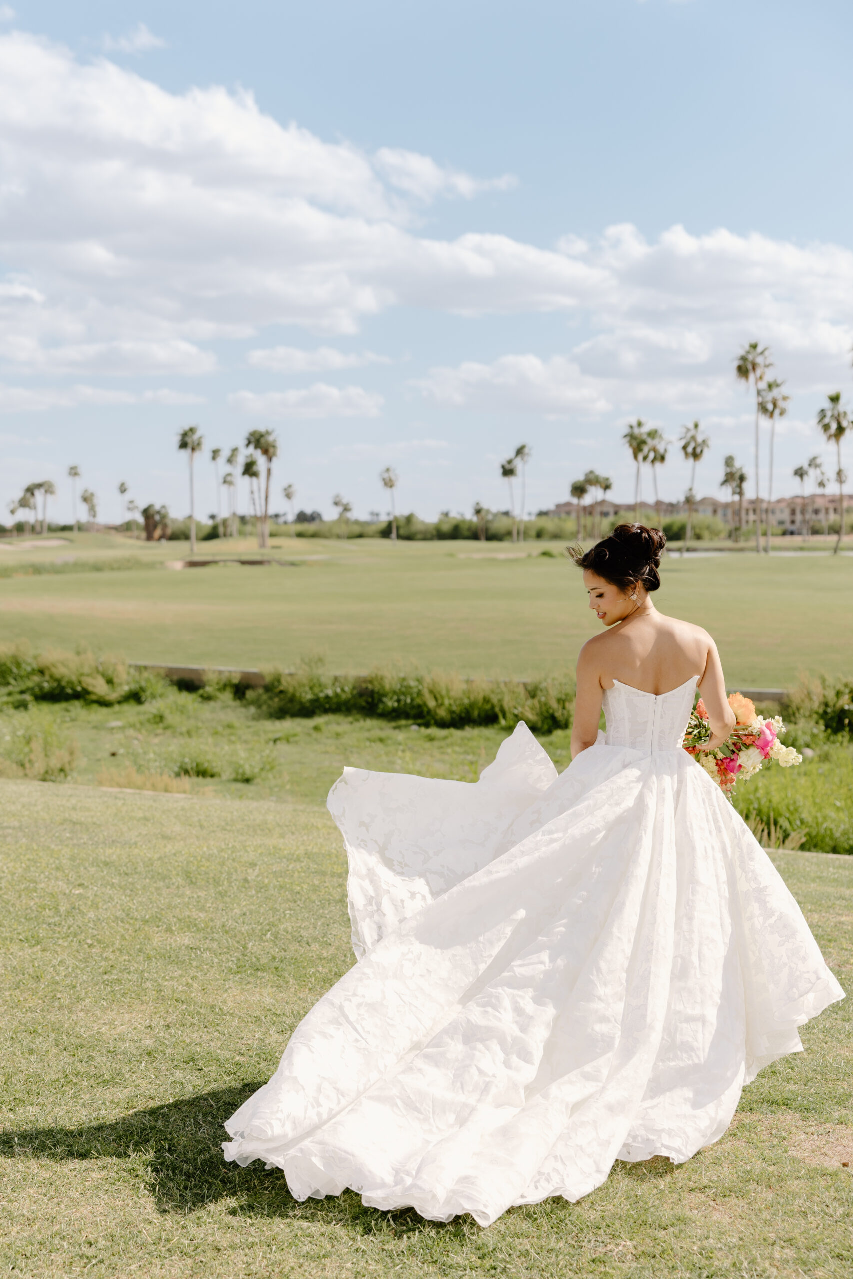 The bride twirling in her flowing lace gown on a sunny lawn, palm trees swaying behind her.