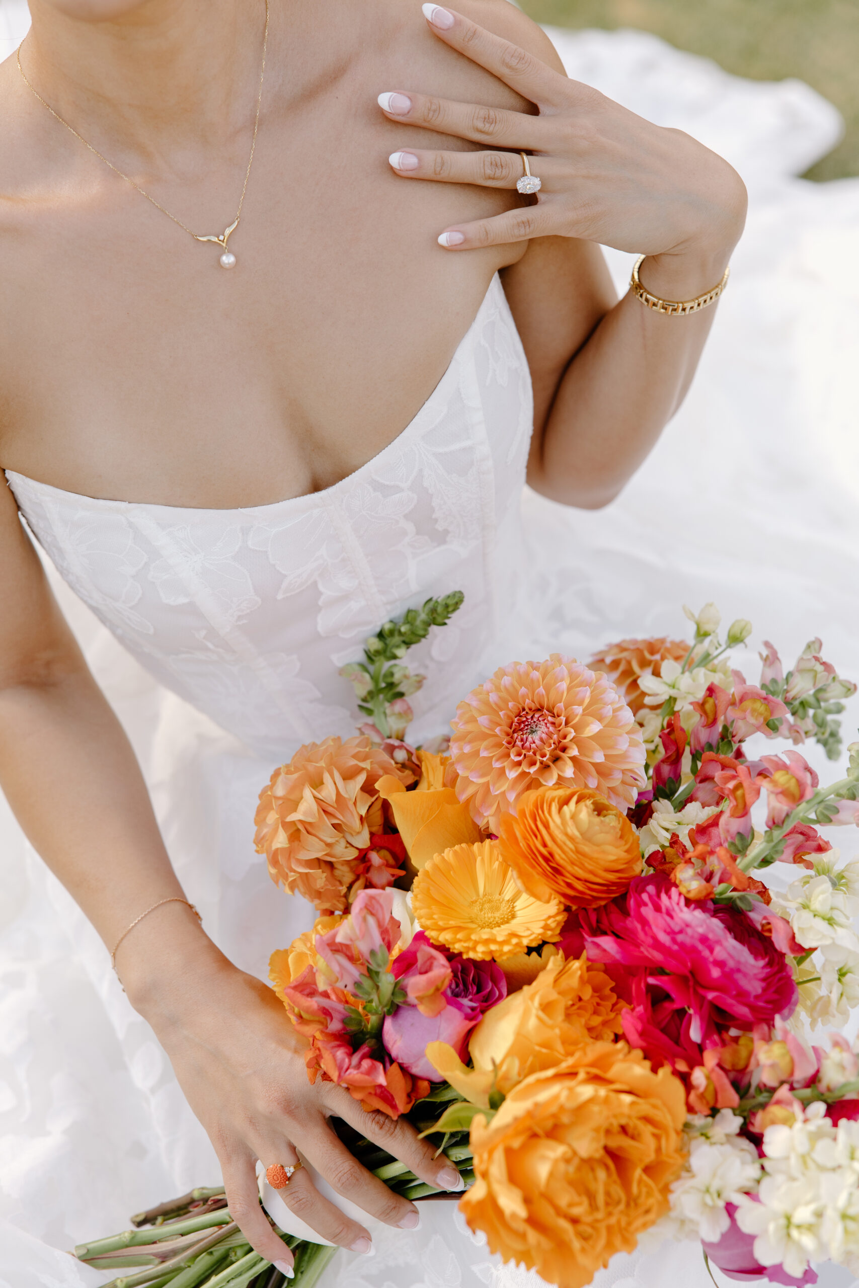 Close-up of a bride holding a vibrant orange and pink bouquet, her lace gown and jewelry glowing in the sunlight at McCormick Ranch Golf Club.