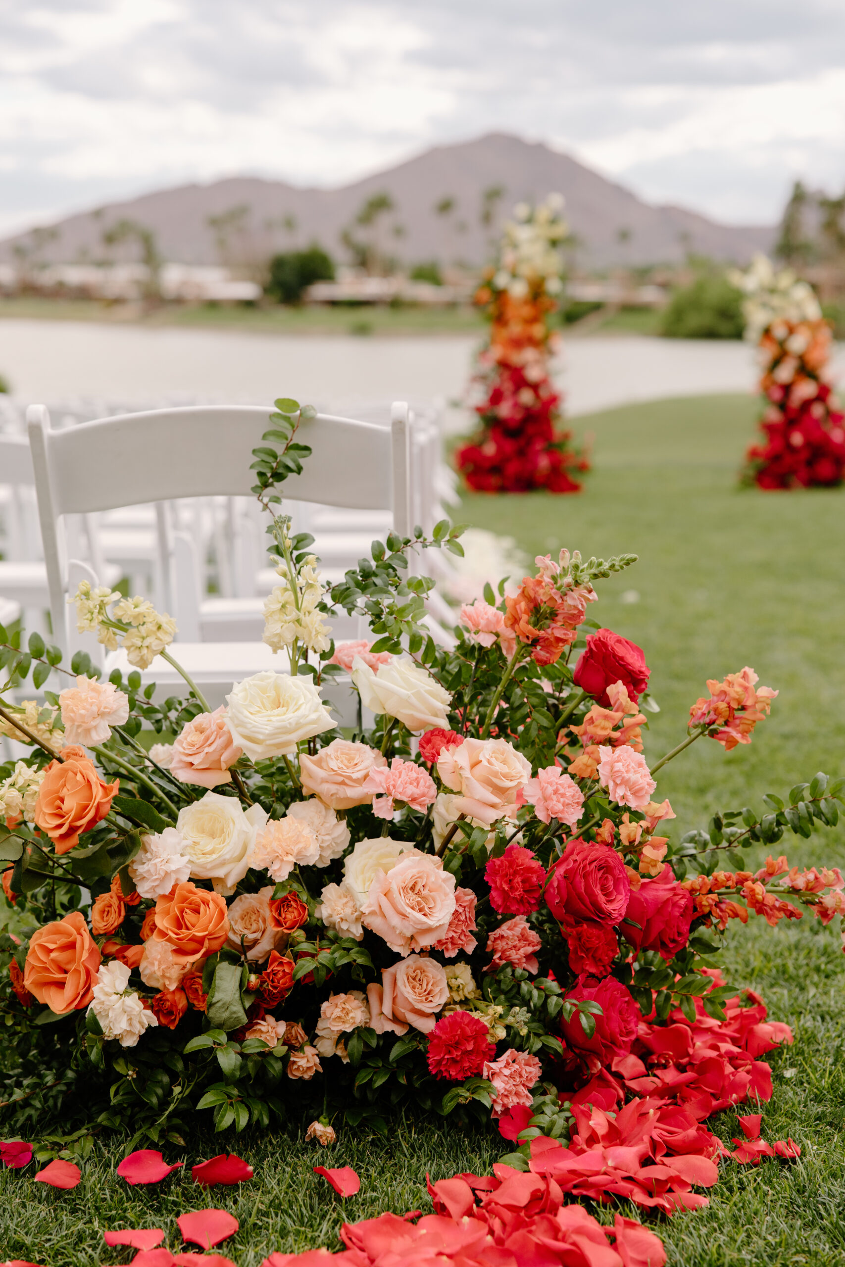 A close-up of lush peach, coral, and red floral arrangements decorating the ceremony aisle.