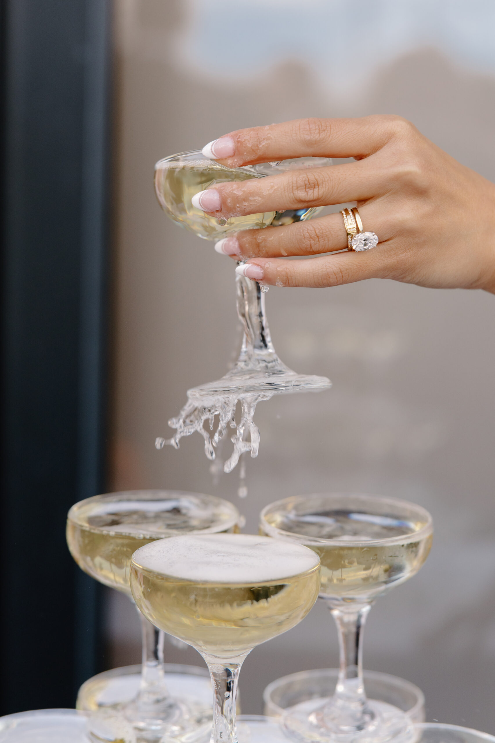 Close-up of the bride’s hand pouring champagne into coupe glasses, her diamond ring sparkling as champagne overflows.