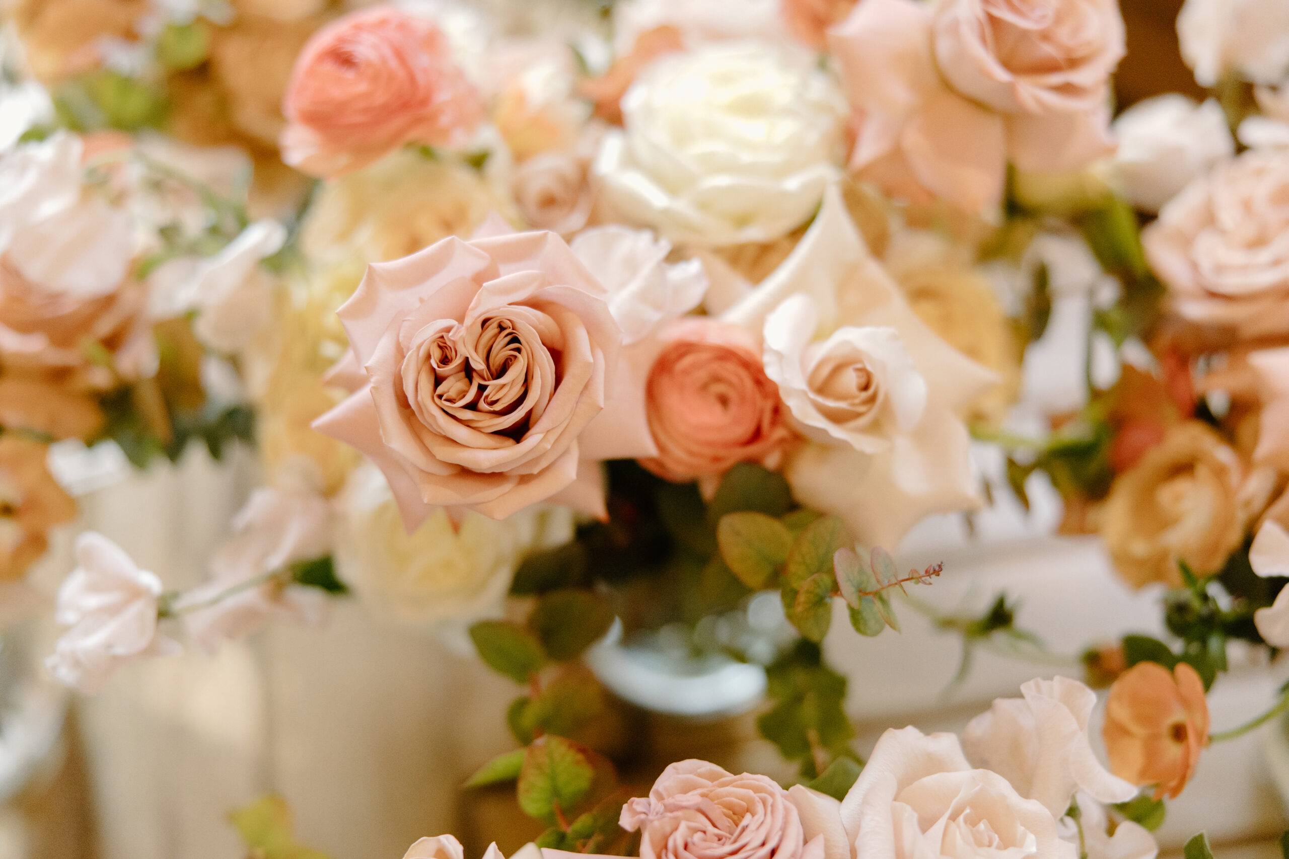 A close-up of a pink peony and roses with greenery softly blurred behind it.