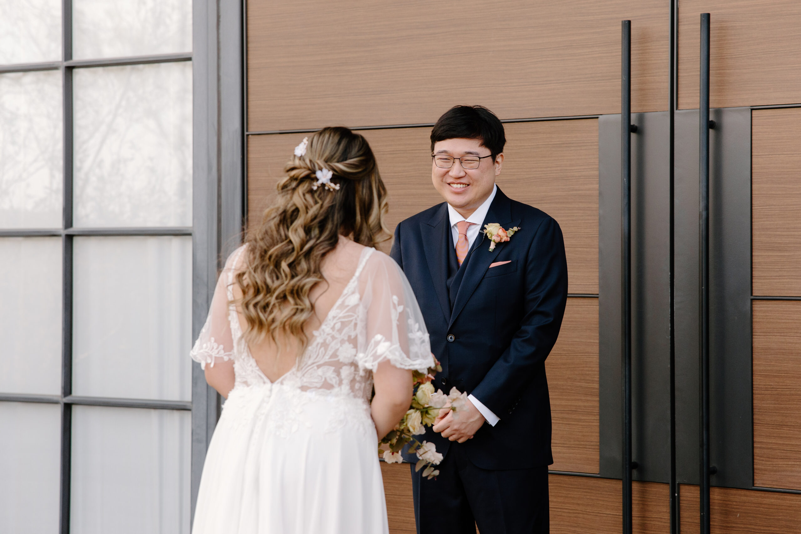 A bride and groom sharing a joyful conversation in front of tall wooden chapel doors, framed by modern desert-venue architecture.