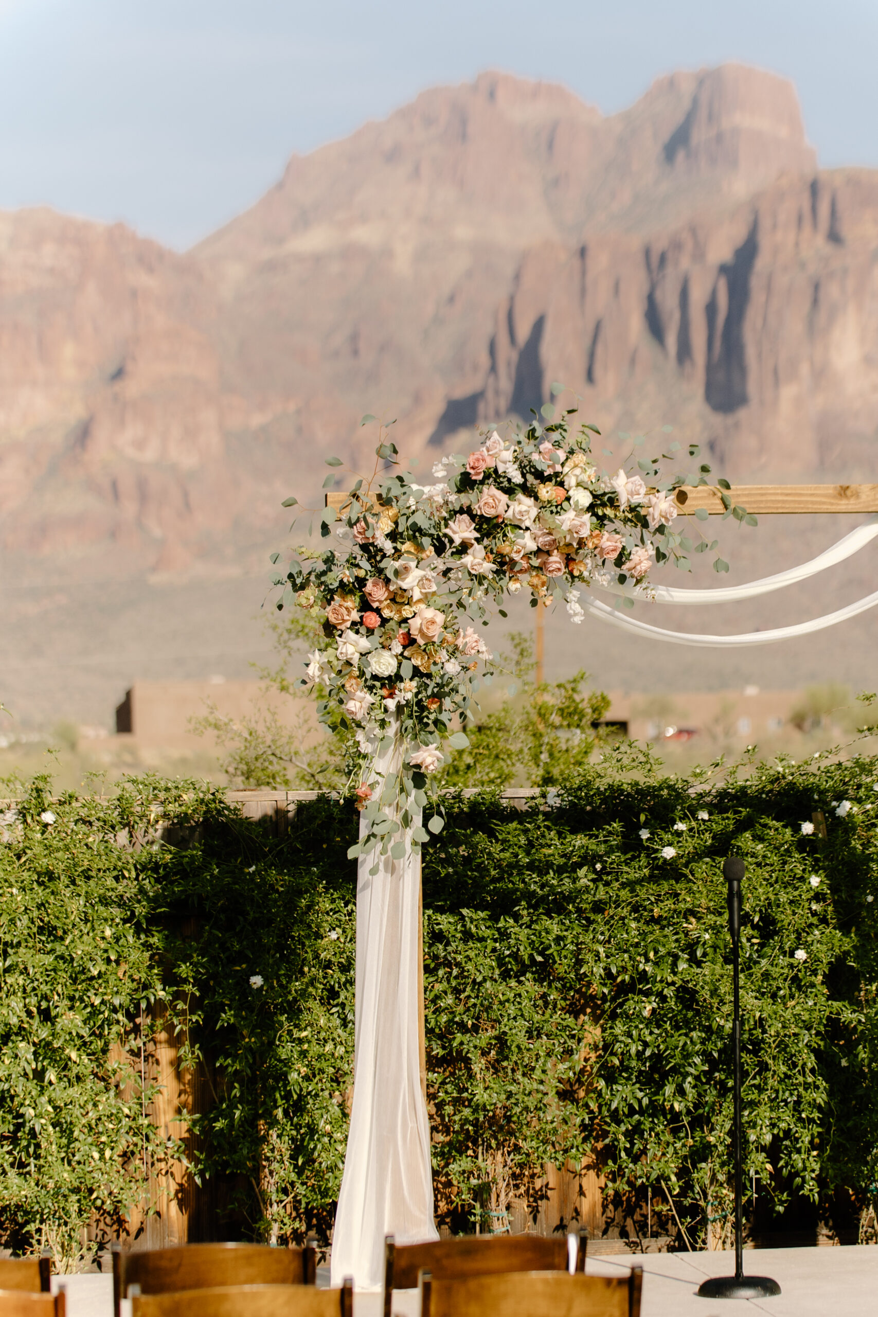 A floral-filled ceremony arch at The Paseo, Arizona, featuring soft pastel roses and greenery with the Superstition Mountains blurred behind it.