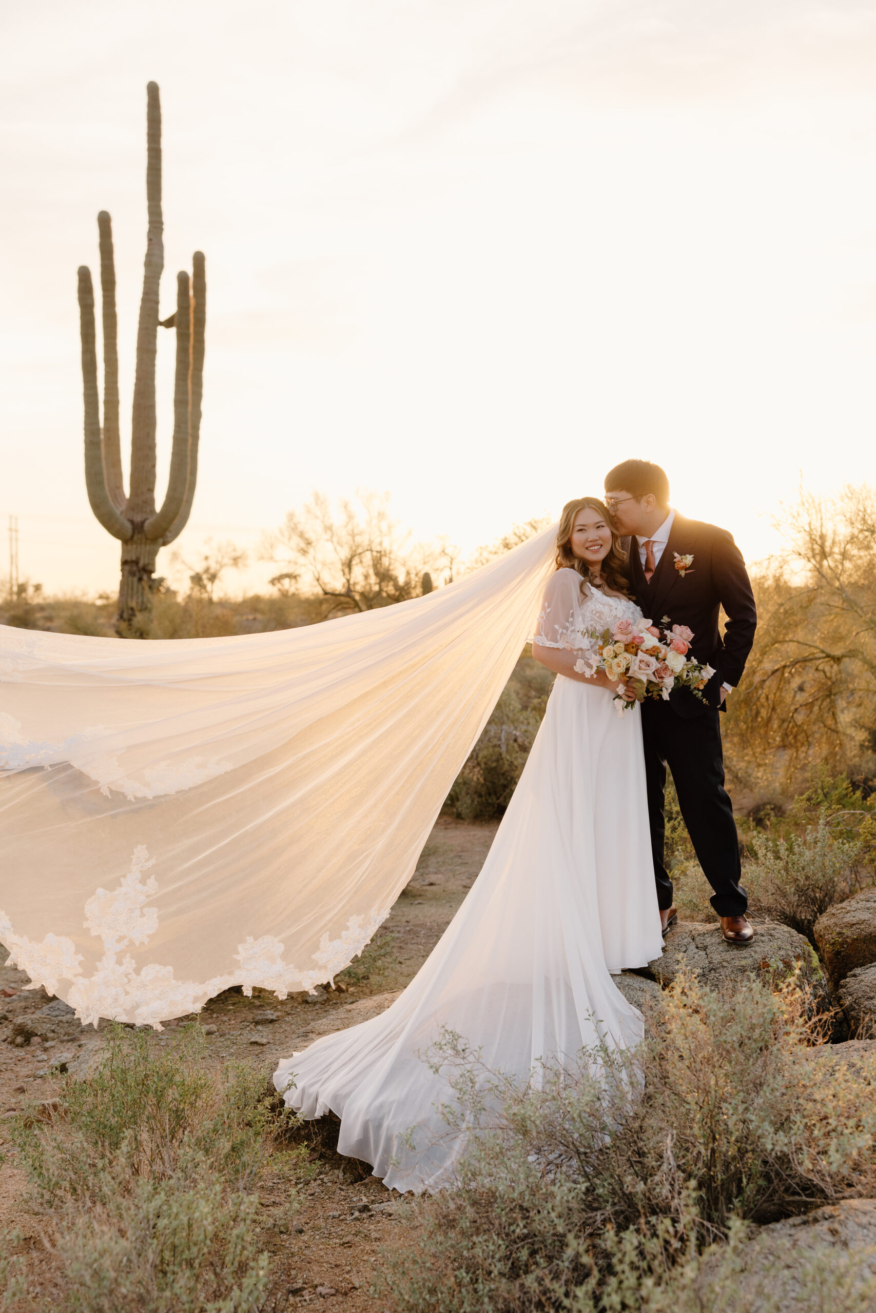 The bride’s veil flowing dramatically behind her during a golden-hour portrait at The Paseo, Arizona, blending airy romance with architectural wood beams.