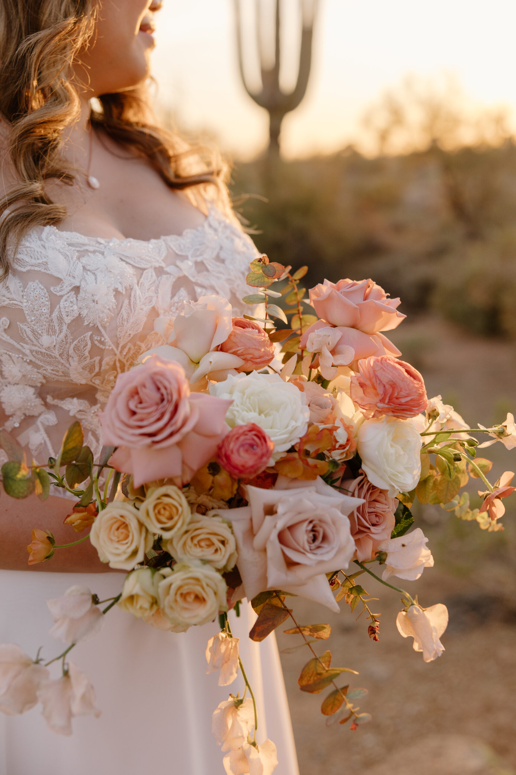 A close-up of soft blush and cream roses arranged in a bridal bouquet, captured in warm, glowing light.