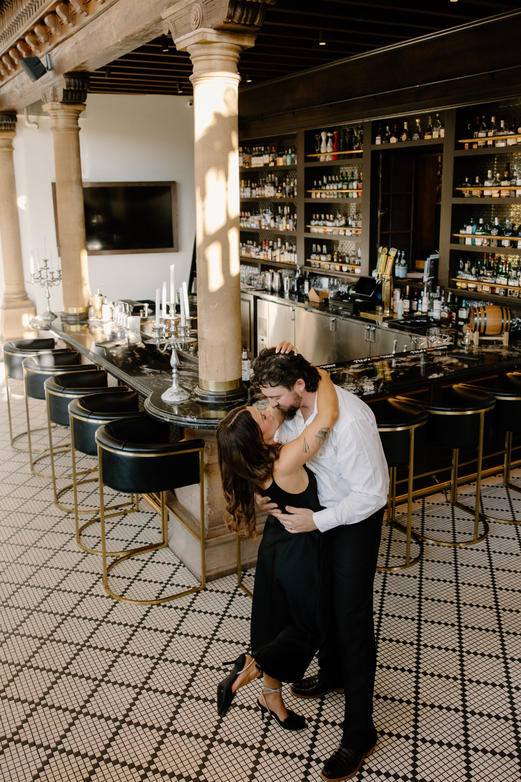 Couple kissing inside an elegant bar with marble countertops, gold barstools, and tiled floors, captured in a romantic indoor proposal setting.