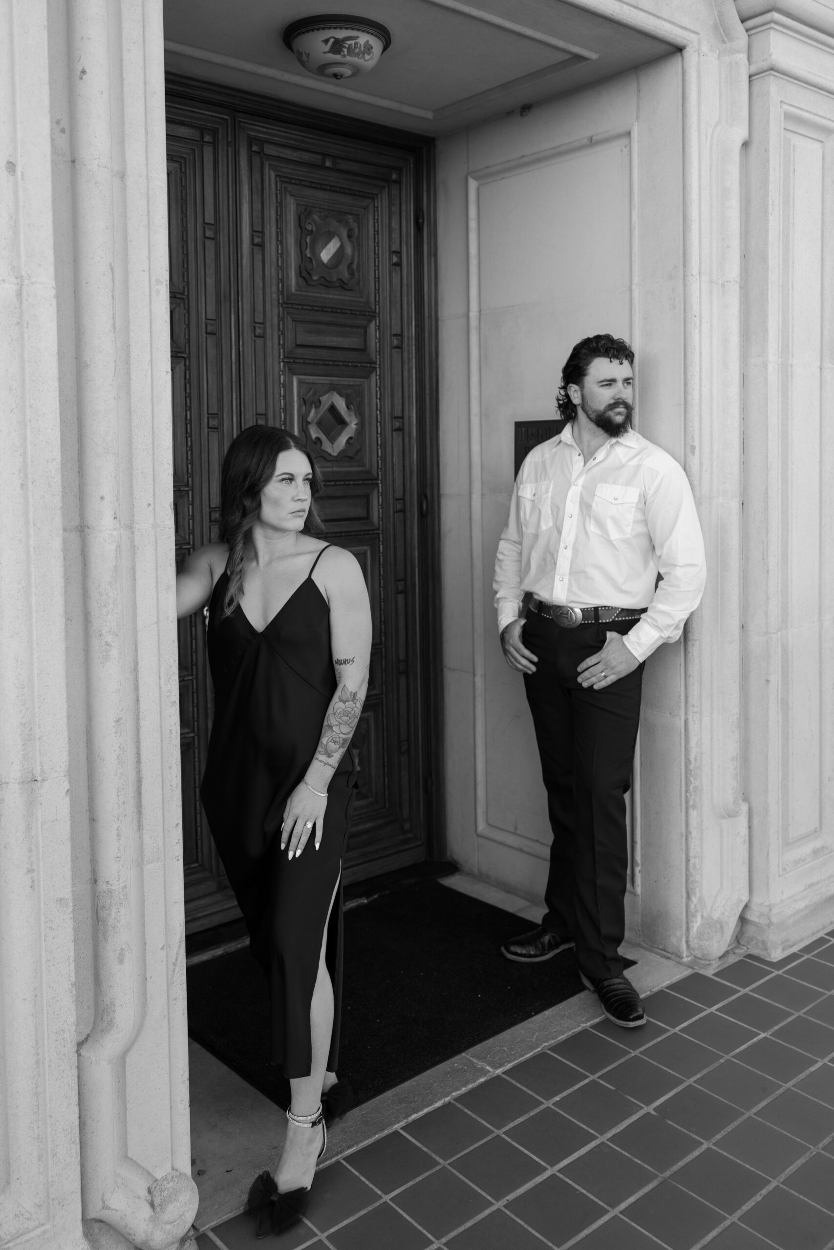 Stylish couple posing in black and white under a historic doorway, capturing a dramatic and timeless downtown Arizona vibe.