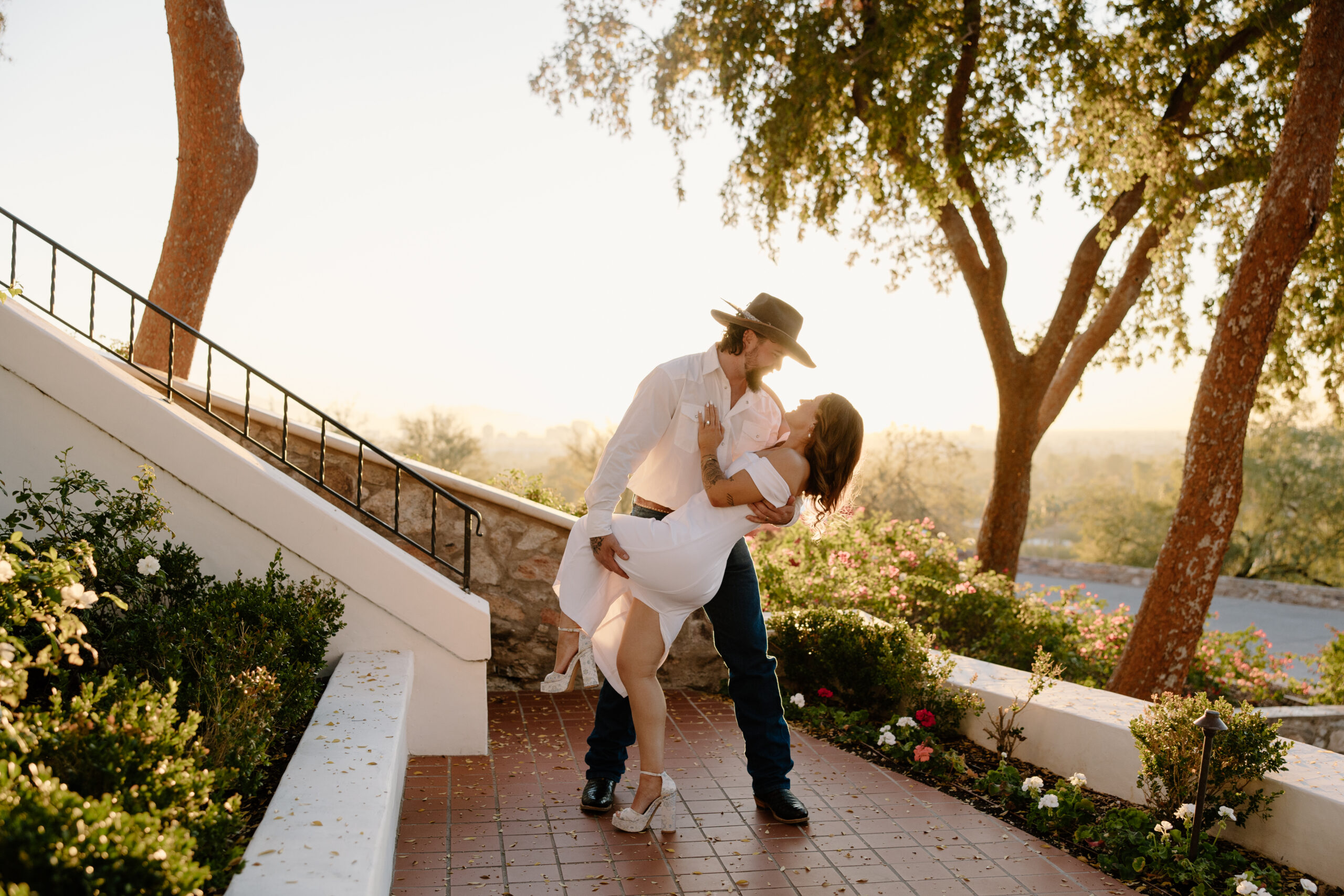 Romantic dip kiss on a tiled terrace surrounded by lush greenery and glowing sunset light, highlighting one of the most intimate Arizona proposal locations.