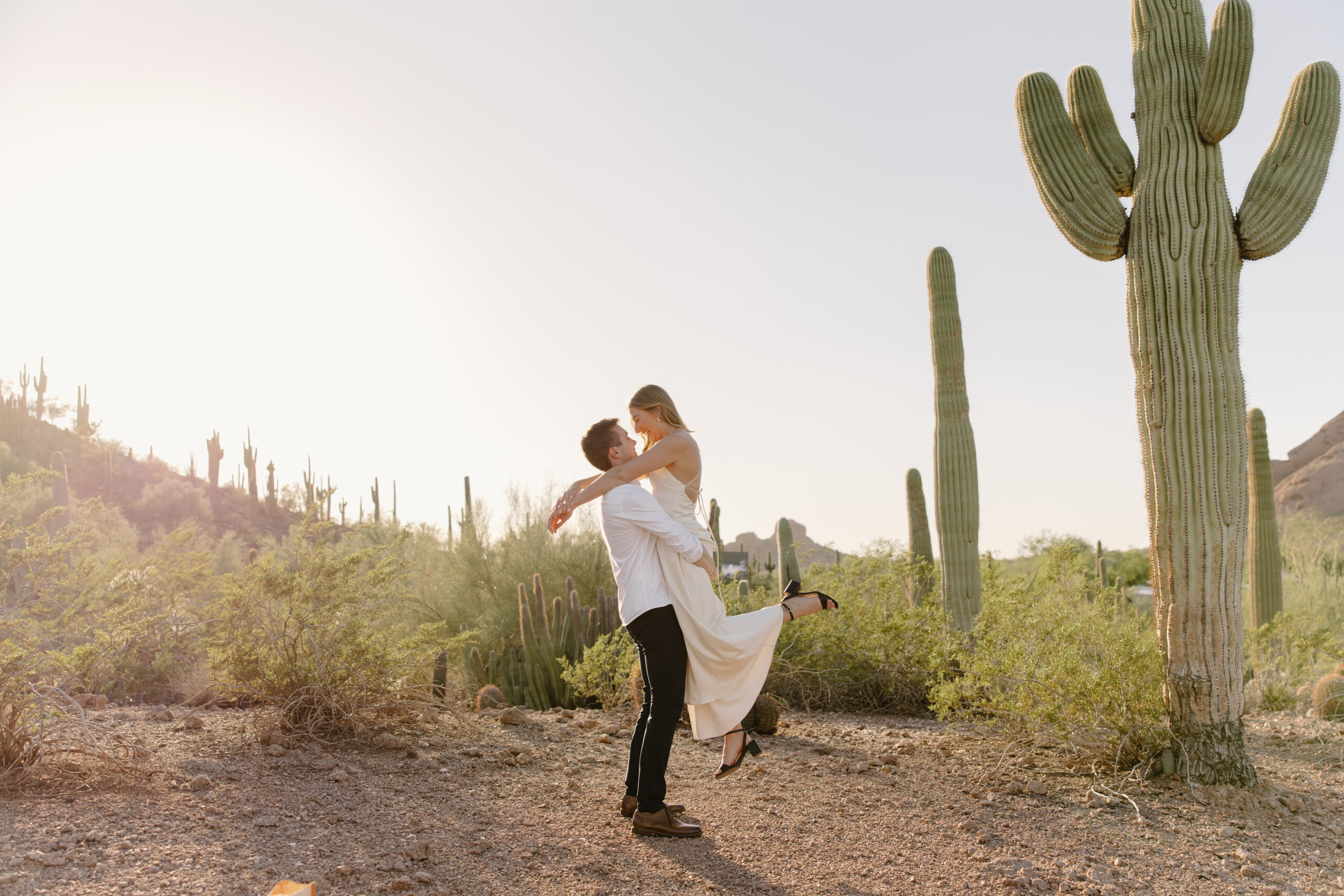 Couple embracing at golden hour in the desert surrounded by tall saguaro cacti, capturing a romantic moment at one of the most iconic Arizona proposal locations.