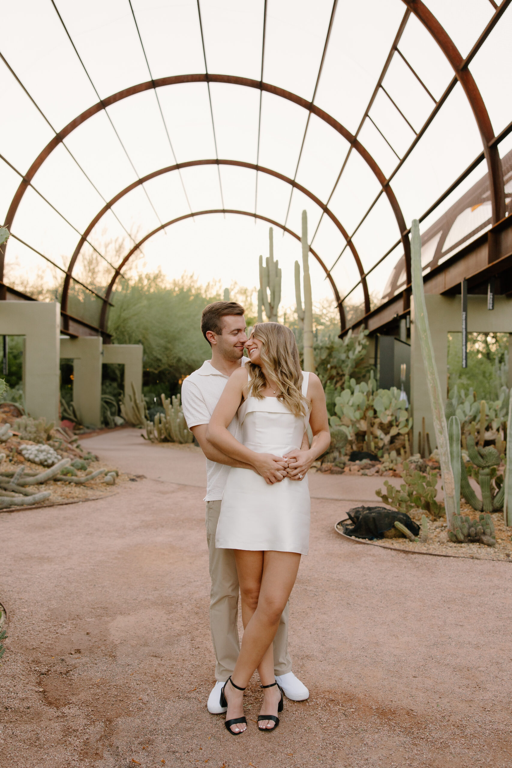 Man hugging his partner from behind among lush cacti and desert greenery in a romantic garden setting perfect for Arizona proposal locations.