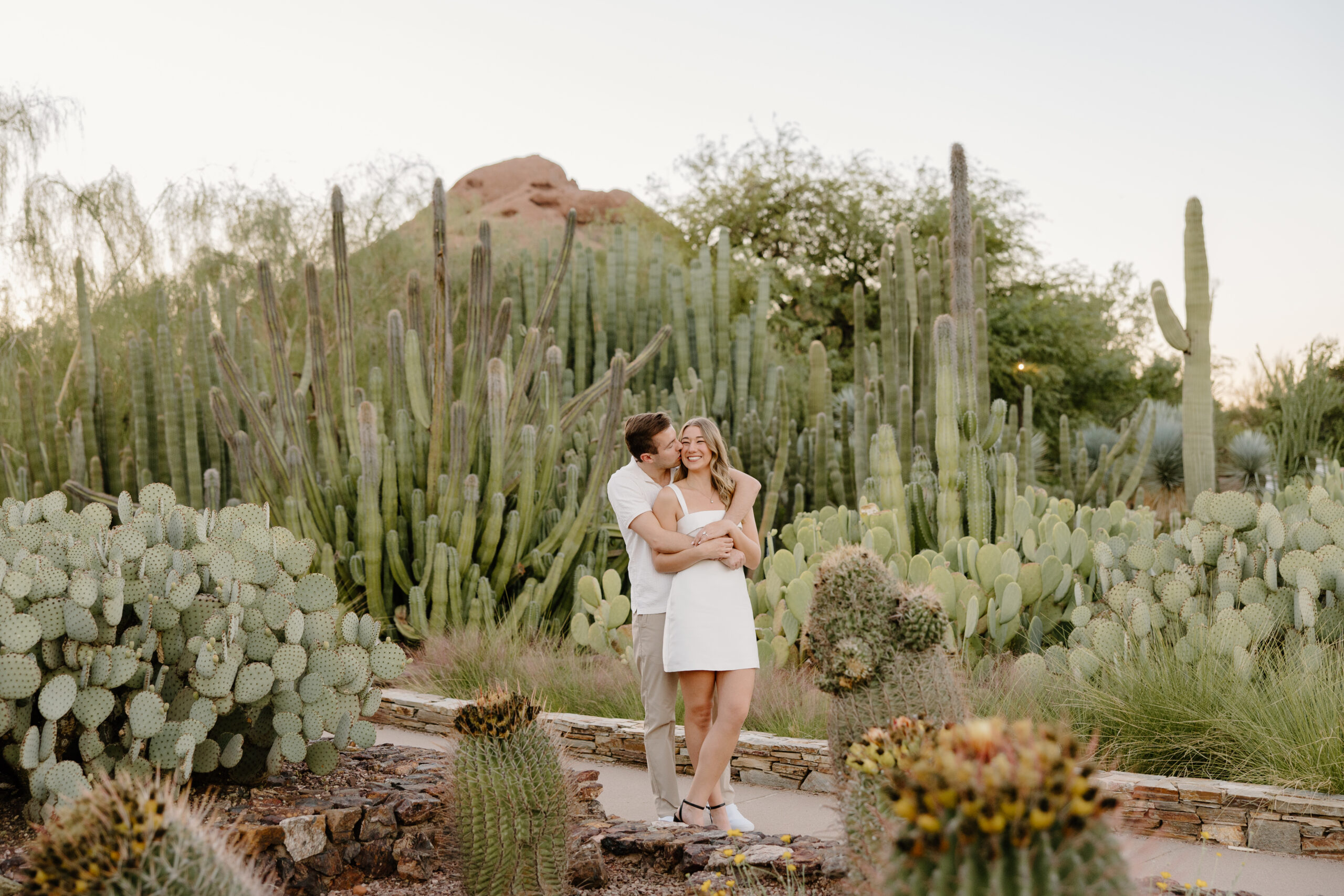 Couple embracing in front of desert cacti and glowing mountain cliffs at sunset, showcasing one of the most breathtaking Arizona proposal locations.