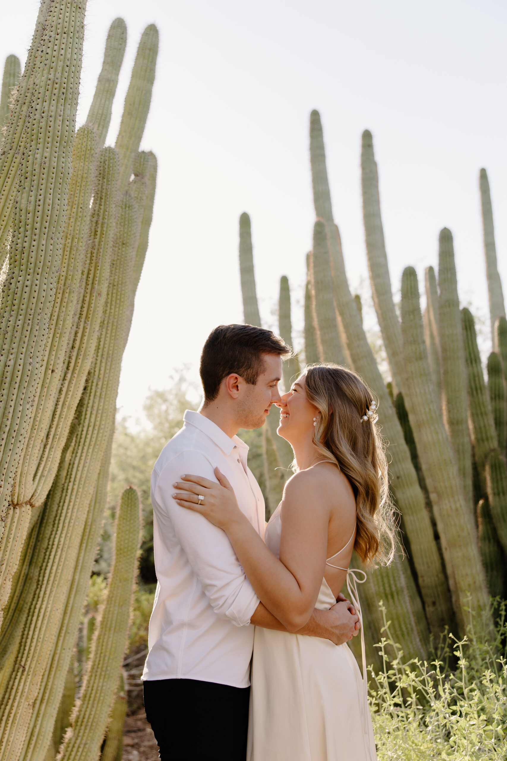 Couple embracing between towering saguaro cacti at golden hour, showcasing the desert beauty that makes Arizona proposal locations so unforgettable.