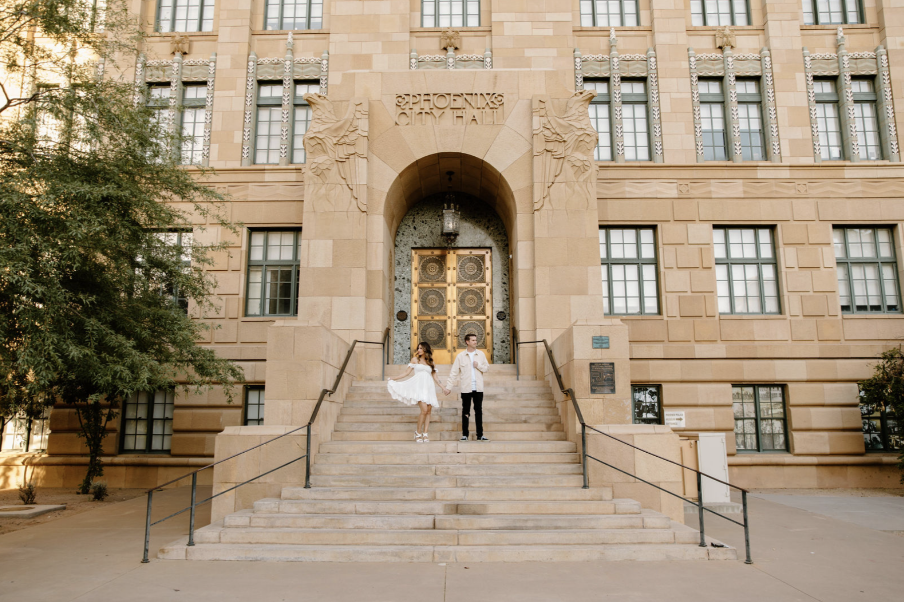 Couple standing on the grand steps of Phoenix City Hall, holding hands in front of ornate gold doors during golden hour at one of the most iconic Arizona proposal locations.