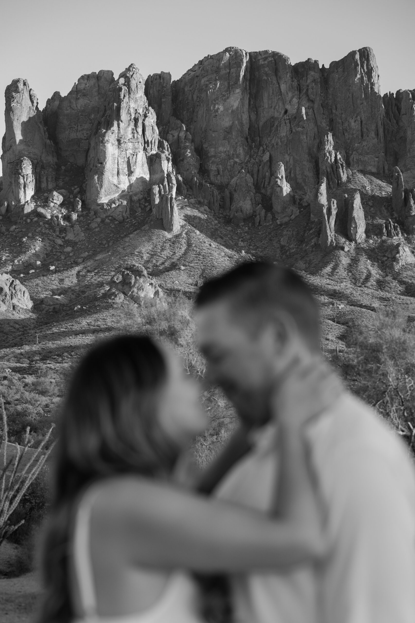Black and white portrait of a couple embracing in front of dramatic desert cliffs, a timeless take on Arizona proposal locations.