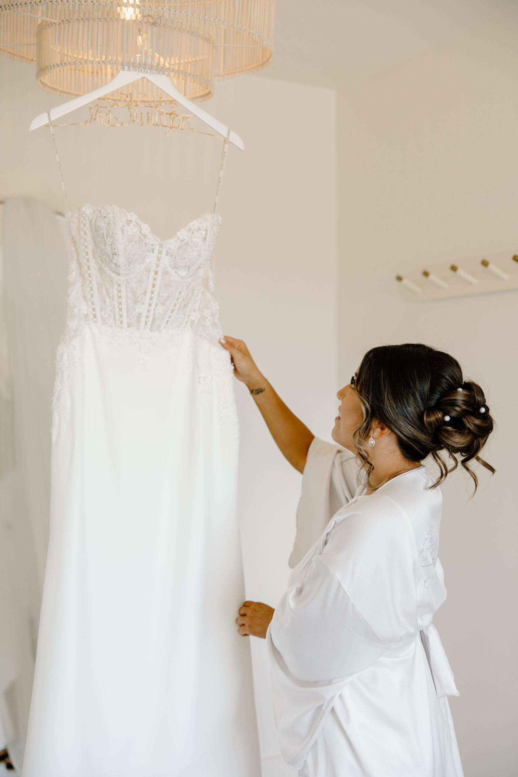 Bride in a silk getting-ready robe admiring her lace wedding dress hanging on a personalized hanger before her Desert View wedding.