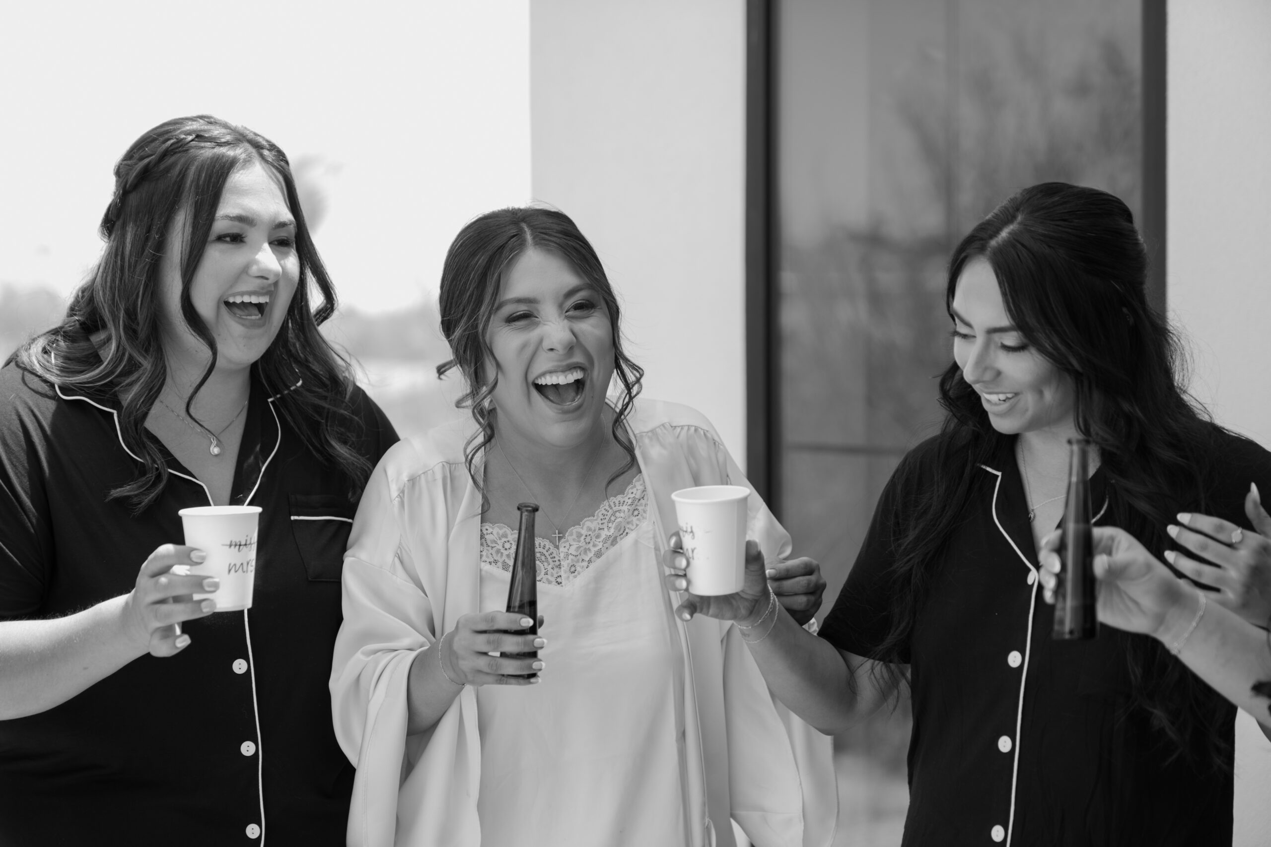 Bride laughing with her bridesmaids while holding drinks during getting ready moments before a Desert View wedding ceremony.