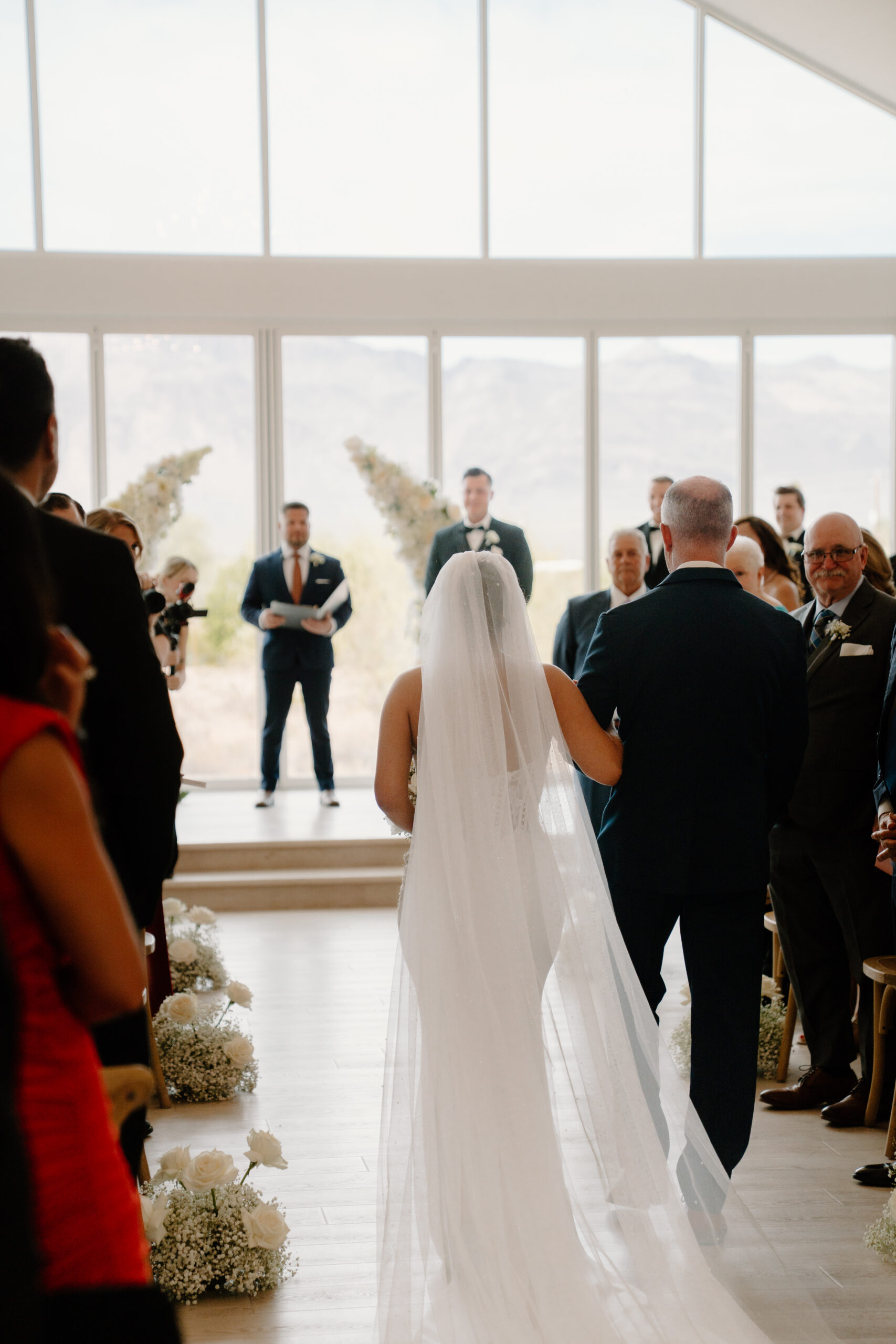 Bride walking down the aisle with her father inside the bright chapel ceremony space with mountain views during a Desert View wedding.