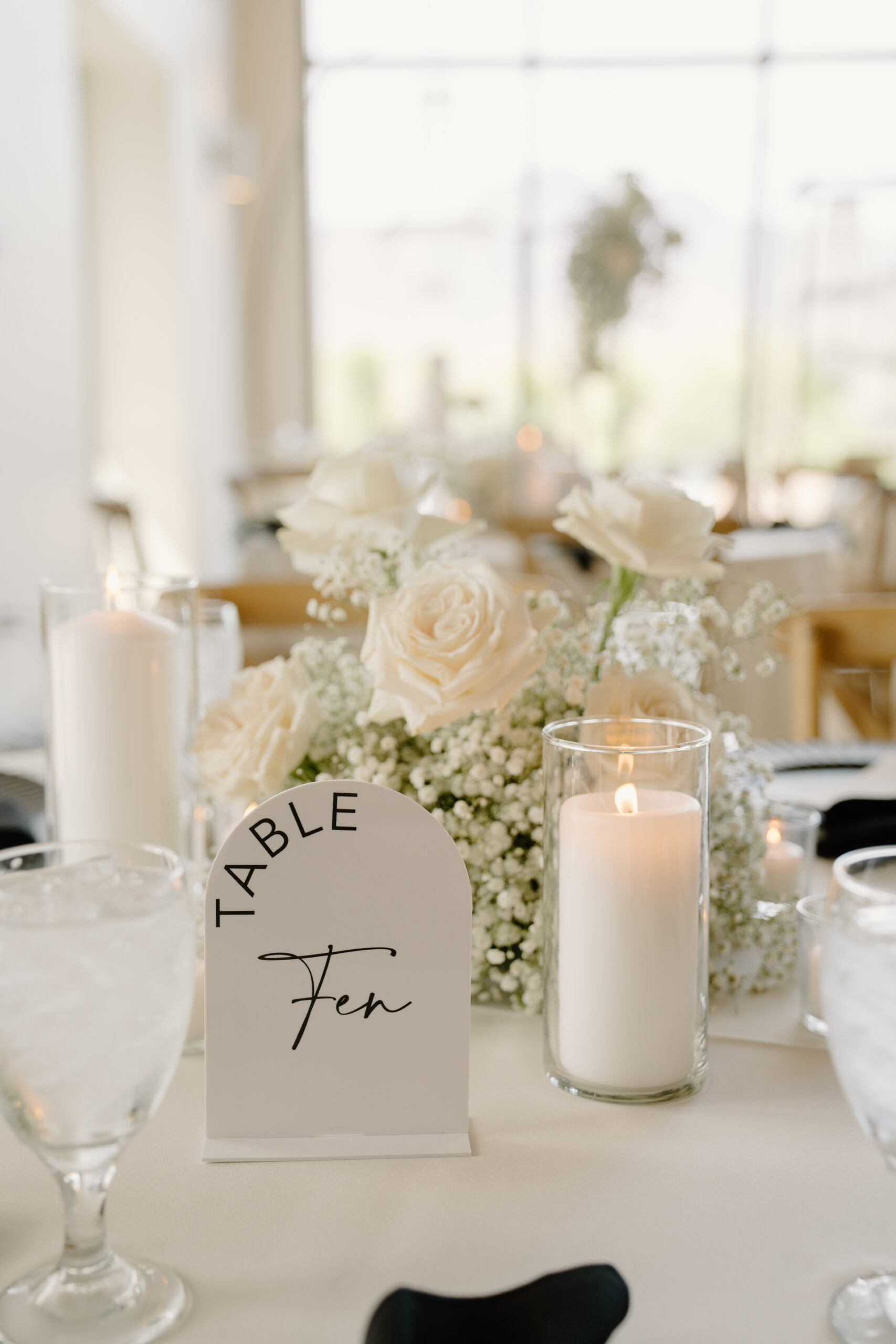 Reception table decor with white roses, baby’s breath, candles, and a “Table Ten” sign at a Desert View wedding reception.