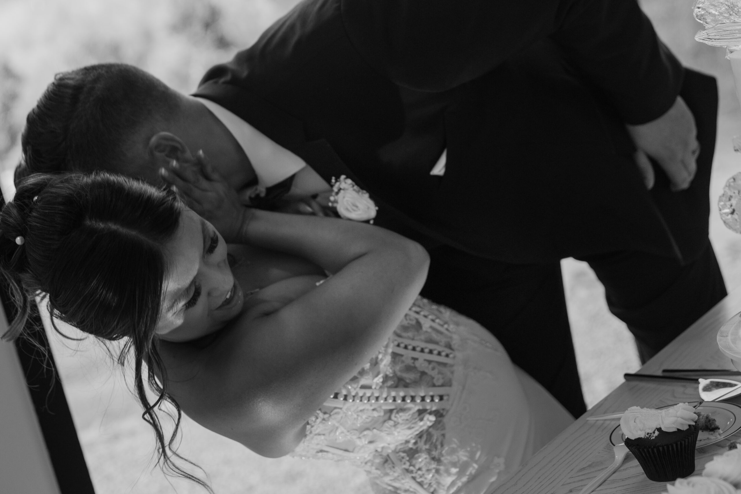 Black and white photo of the bride leaning over the groom while feeding him a bite of cake during their Desert View wedding reception.