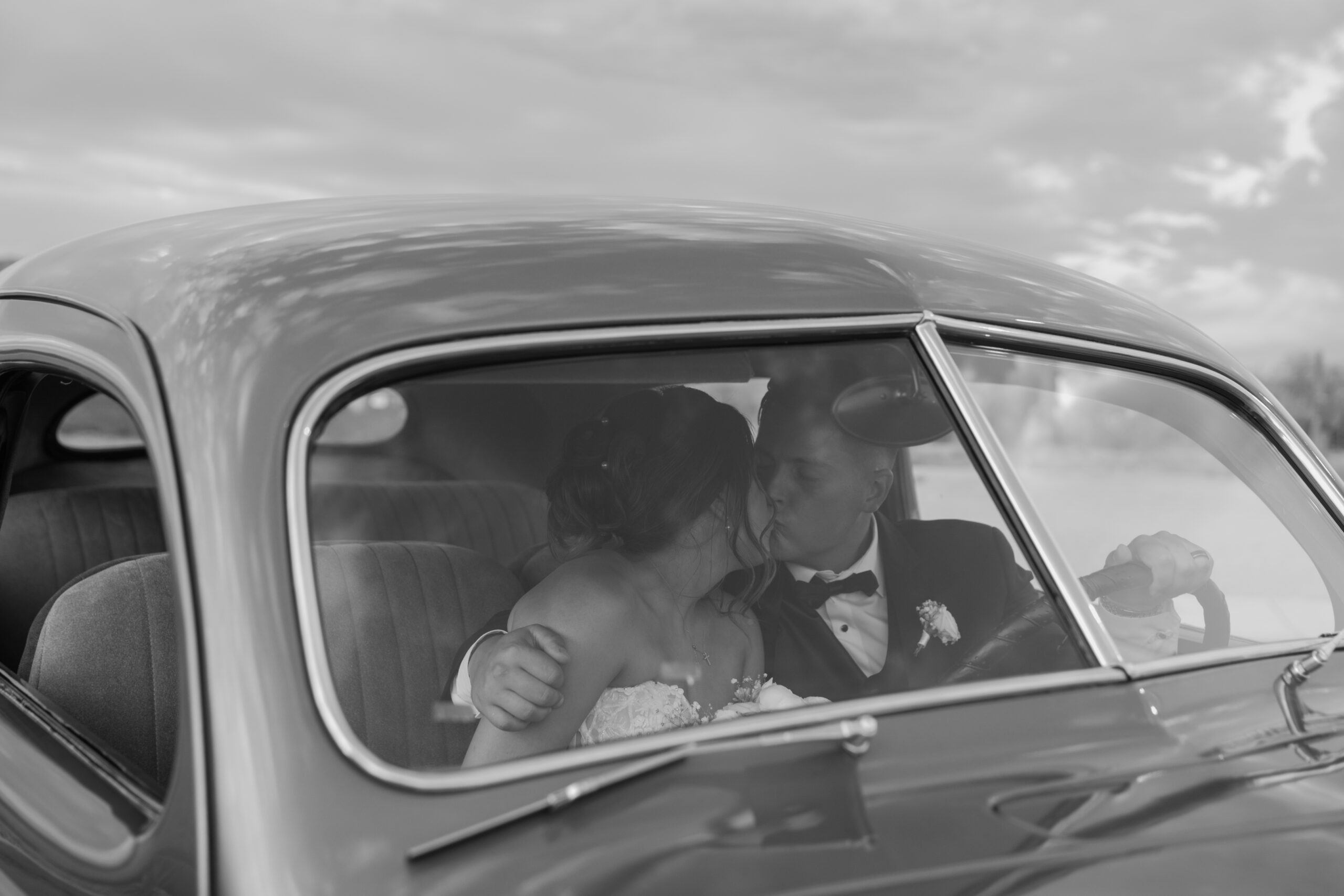 Black and white photo of the bride and groom kissing inside a vintage car after their Desert View wedding.