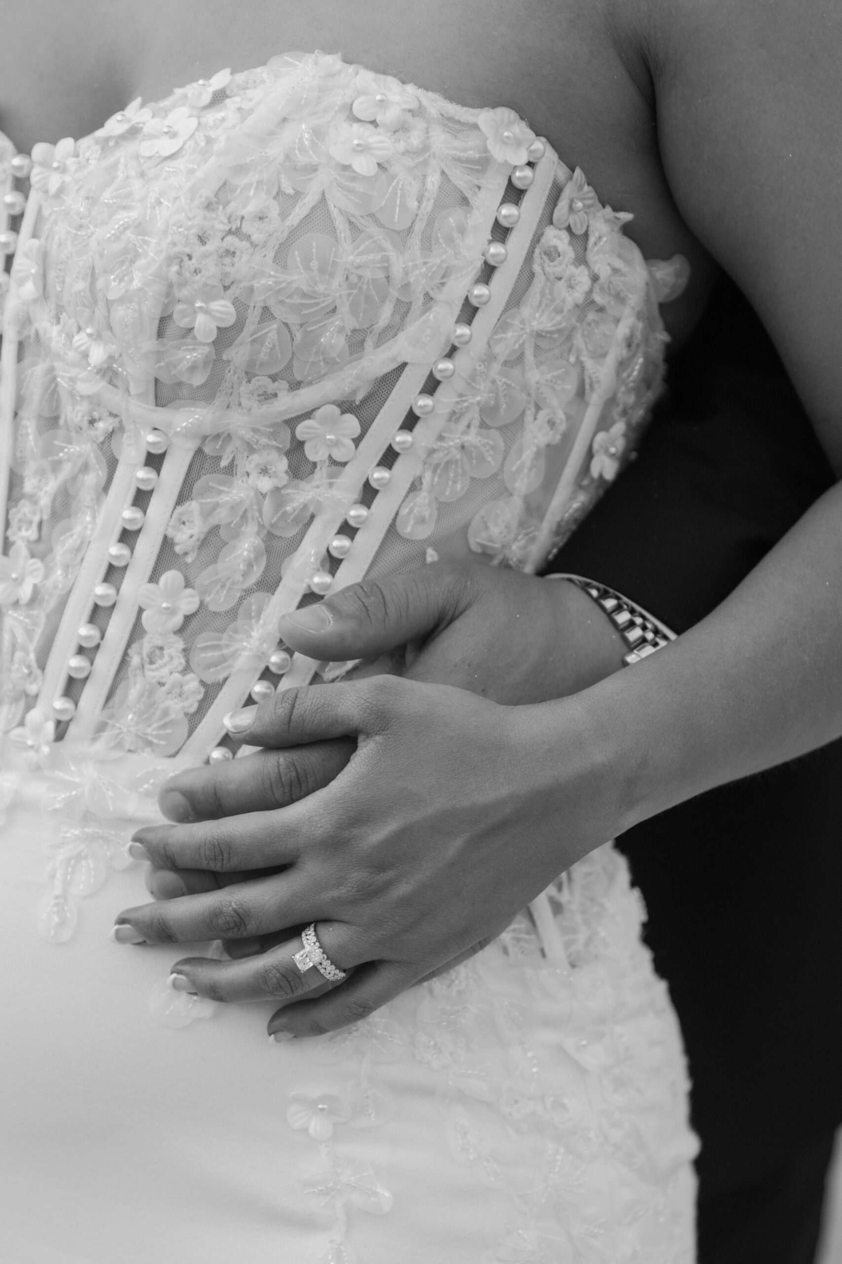 Close-up detail of the bride’s floral lace wedding dress bodice with pearl embellishments and her engagement ring resting on her hand.