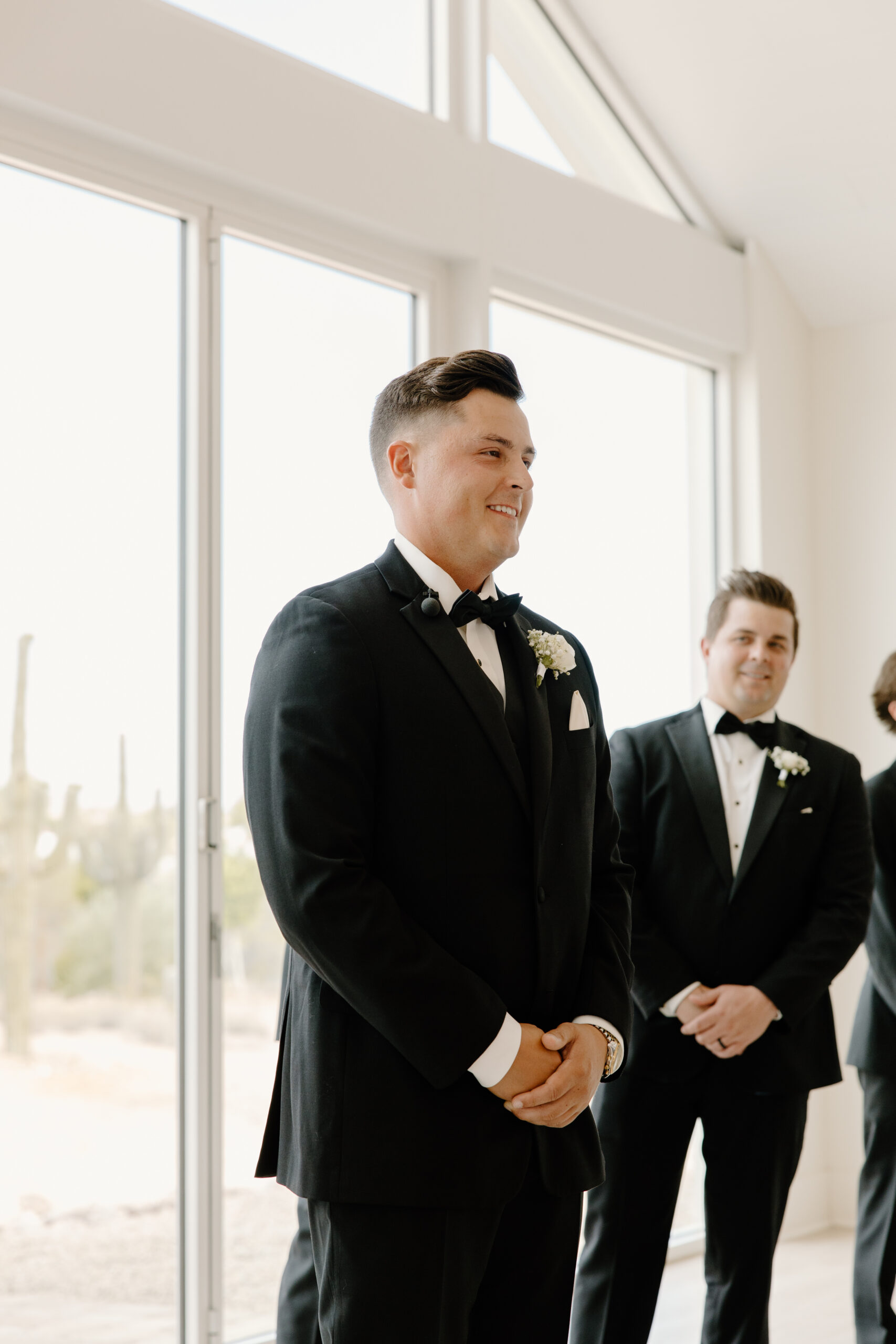 Groom smiling during the ceremony while standing at the front of the chapel with groomsmen beside him.
