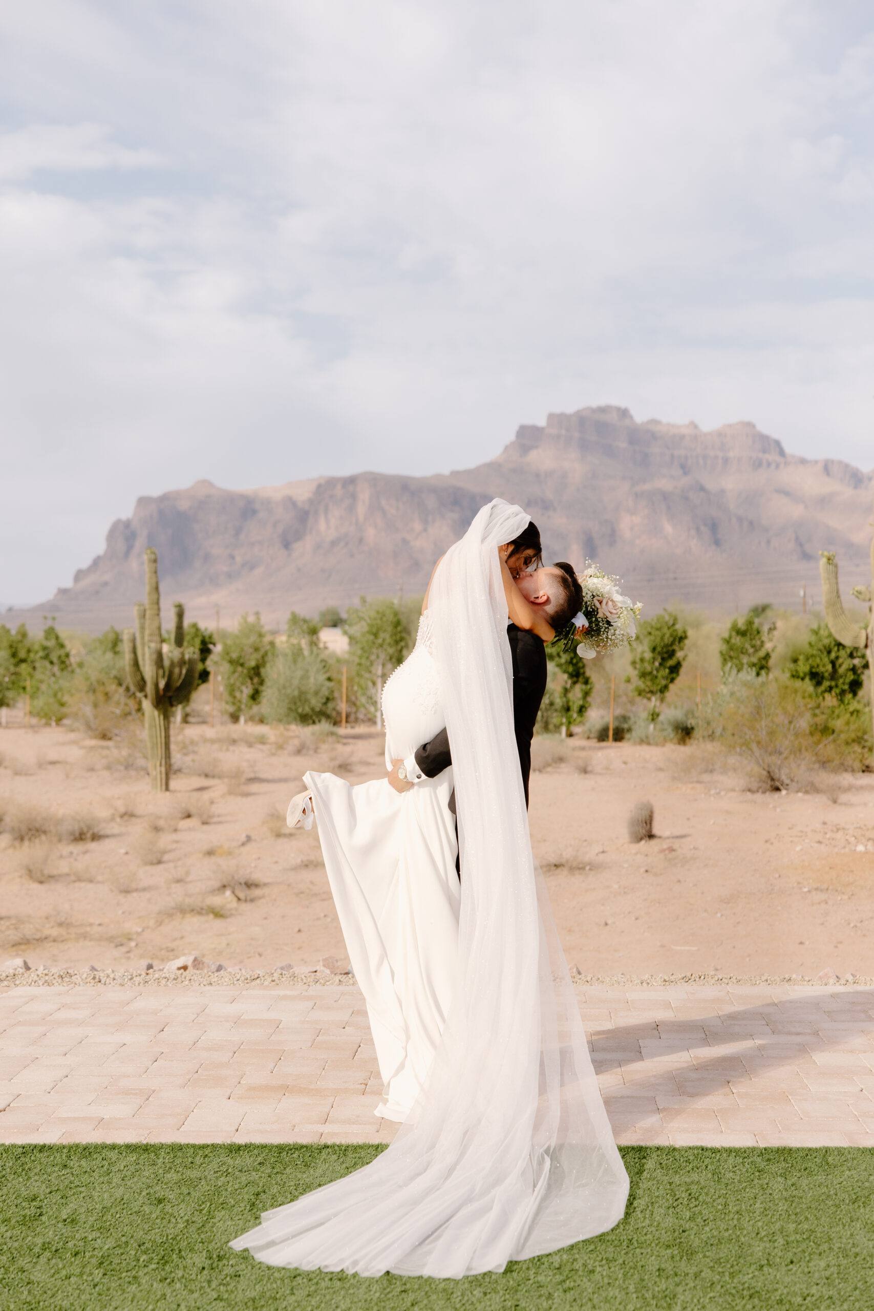 Bride and groom sharing a kiss outside with desert mountains and saguaros behind them after their Desert View wedding ceremony.