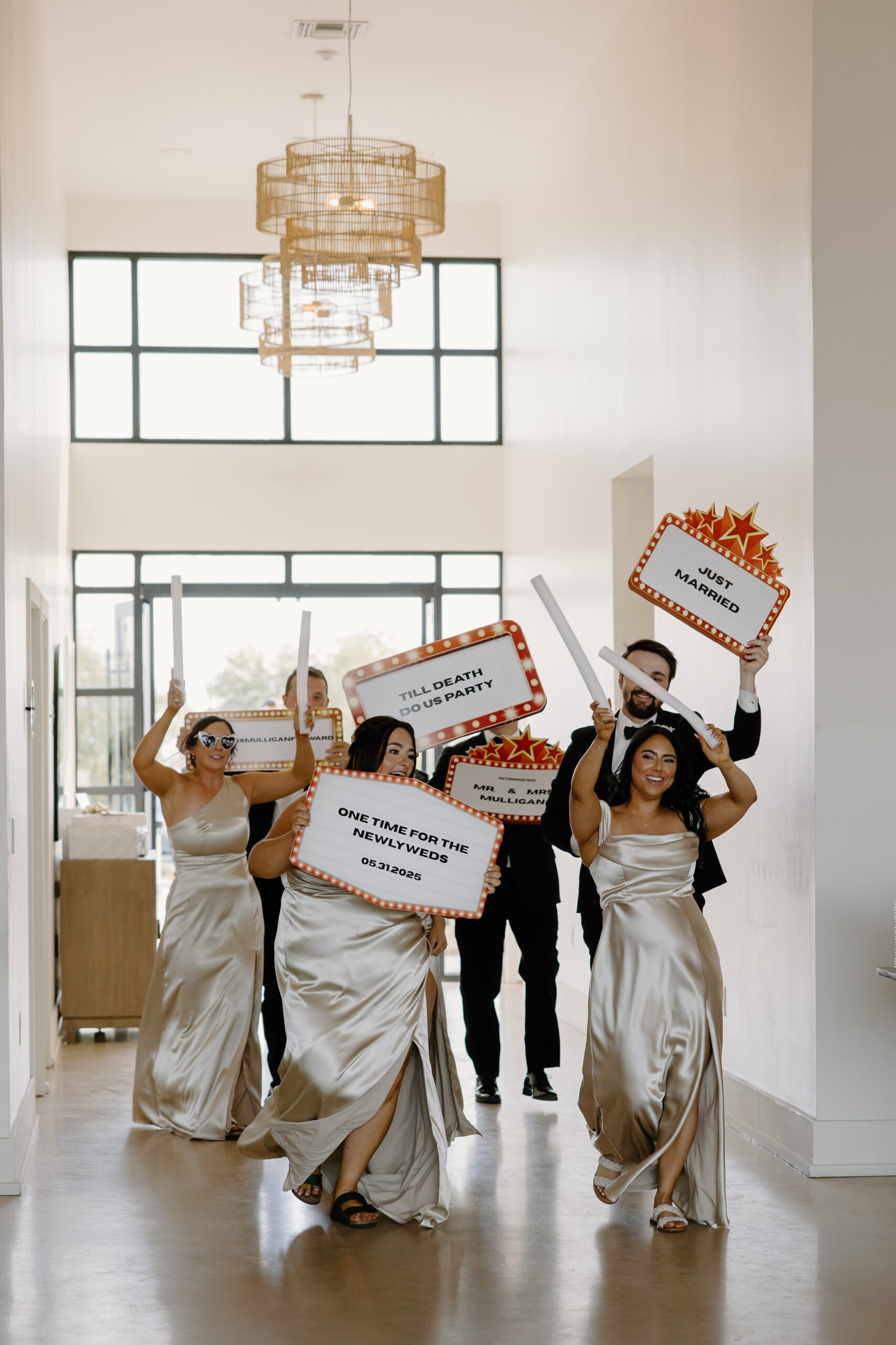 Bridesmaids and friends entering the reception holding fun wedding signs and glow sticks.