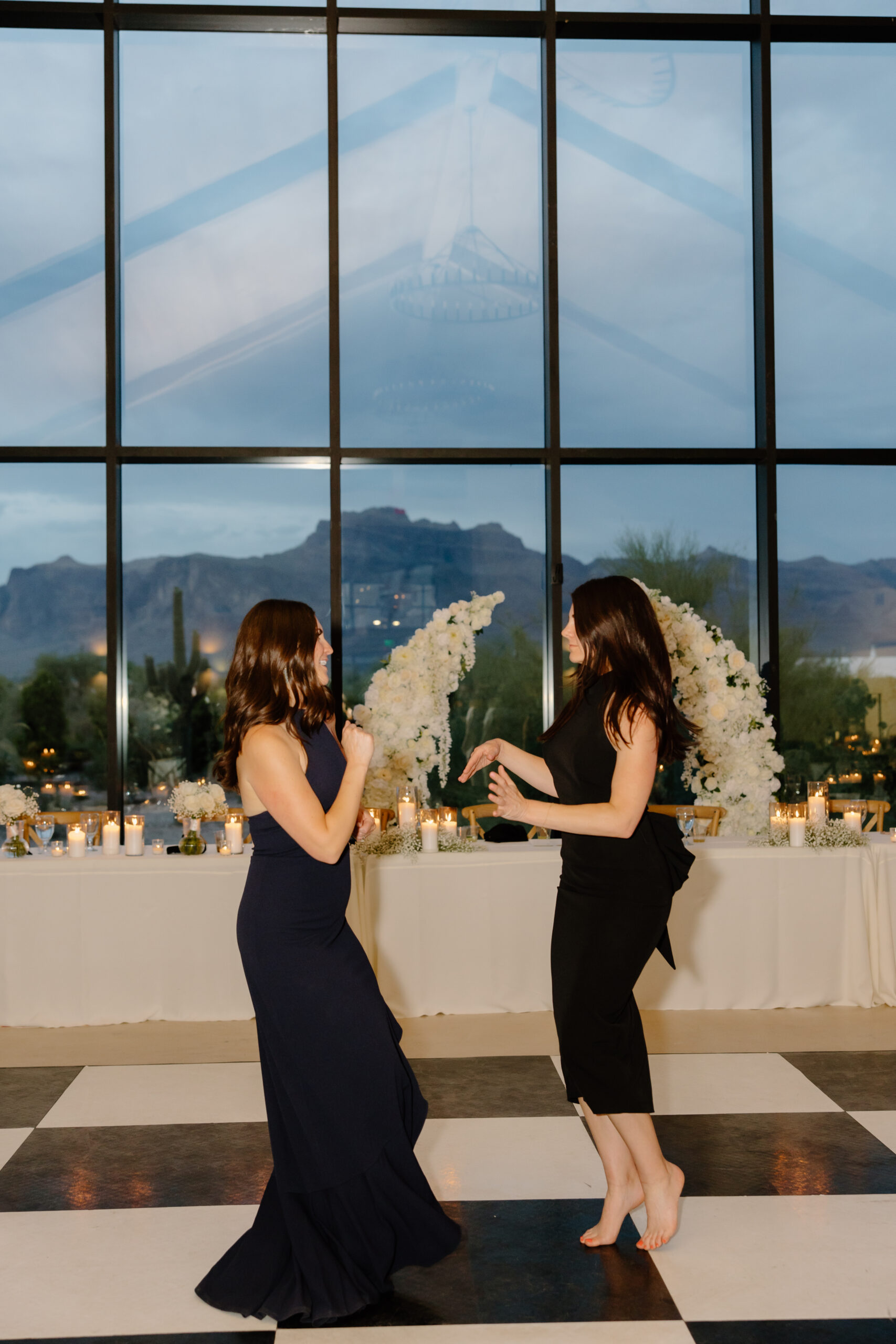 Two guests dancing together on the checkered dance floor with candles and floral arrangements behind them at a Desert View wedding reception.